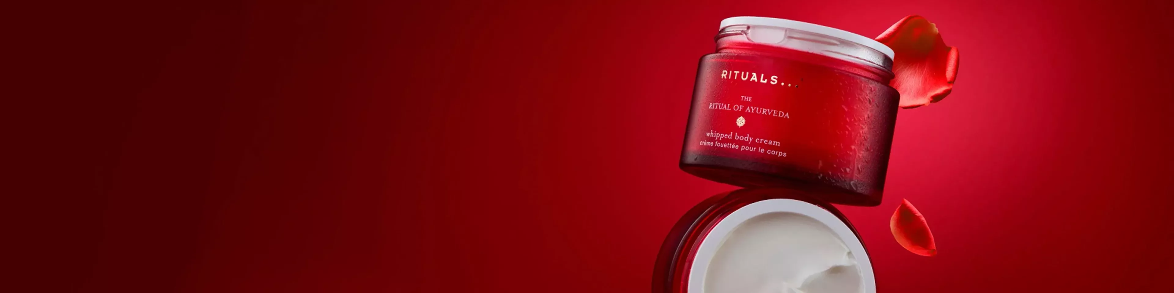 Rituals The Ritual of Ayurveda whipped body cream jar with lid off, red background and rose petals