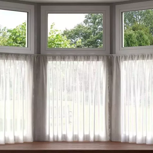 Bay window with sheer net curtains and grey drapes, letting in natural light with garden view outside