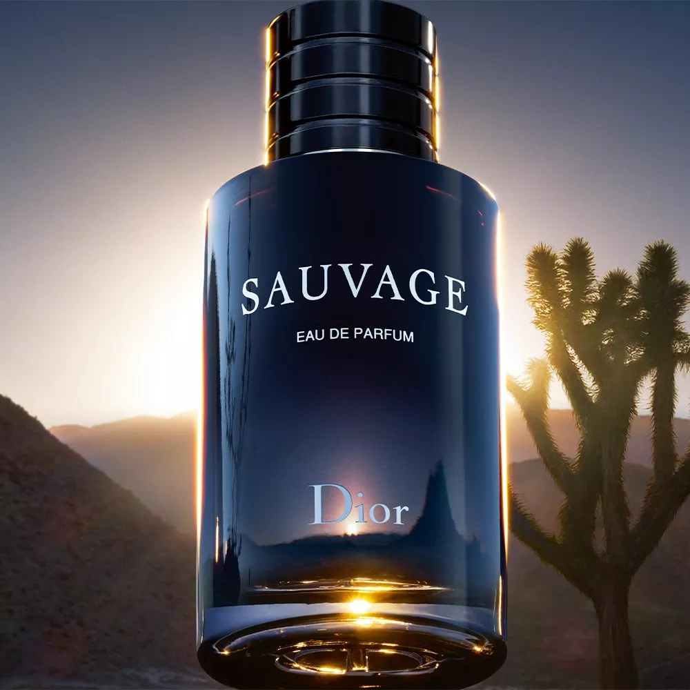 Dior Sauvage Eau de Parfum bottle close-up with desert mountains and cactus at sunset, luxury fragrance advert
