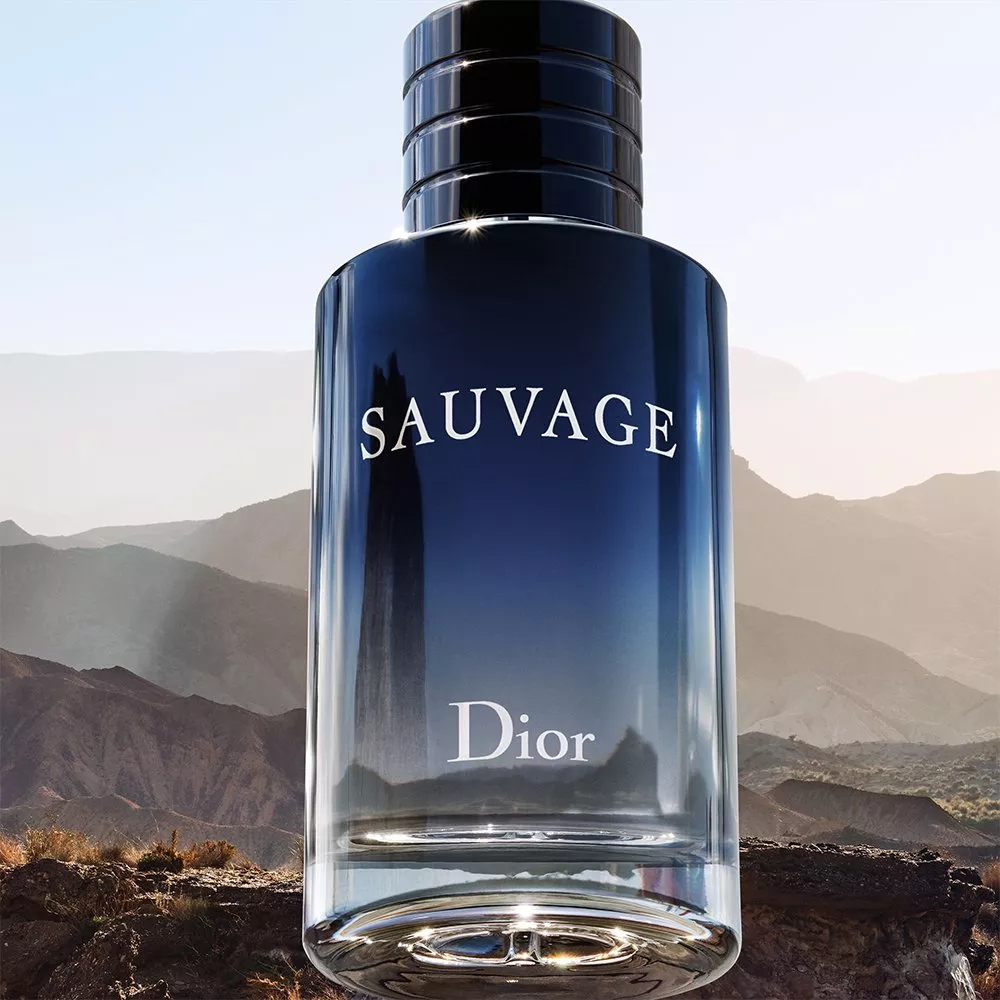 Dior Sauvage men's aftershave bottle in blue glass, close-up product shot with mountain landscape backdrop