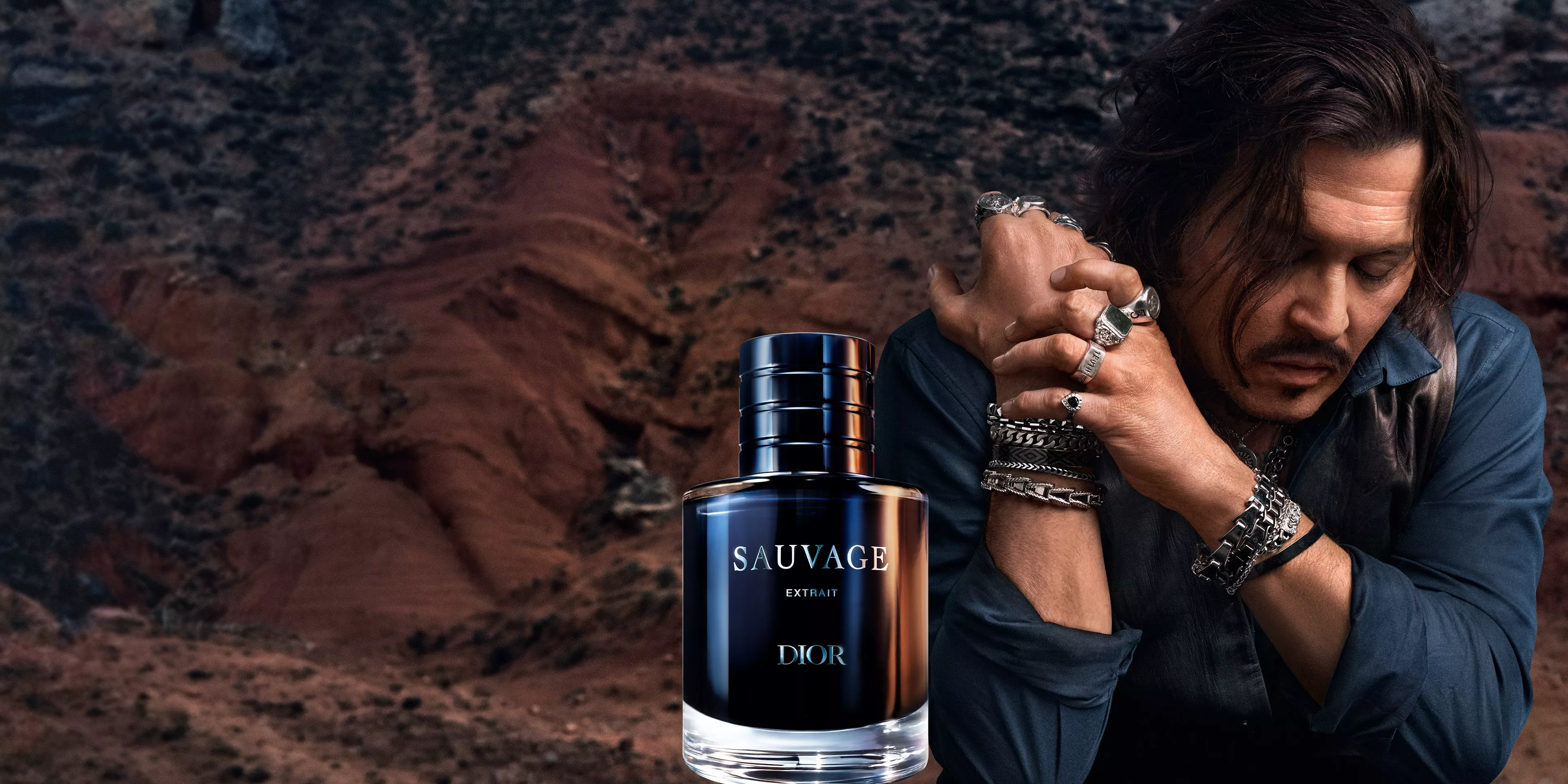 Dior Sauvage Extrait perfume bottle with rugged desert backdrop and pensive male model in jewellery, close-up