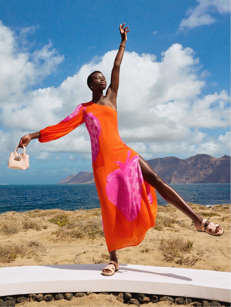 women in a bright orange dress stretching out to the blue sunny sky