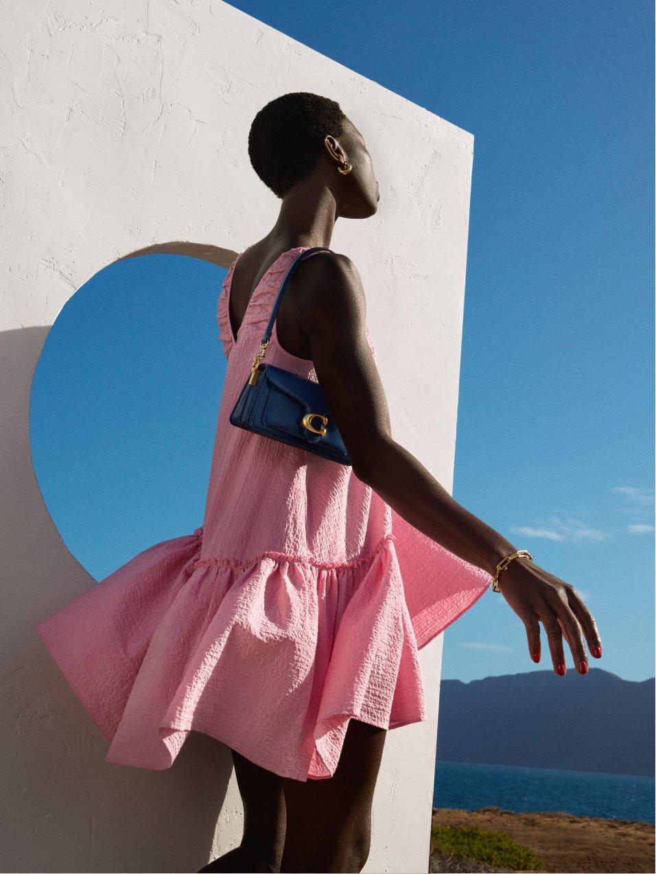 Woman in dink dress looking out to horizon of a sunny rocky landscape