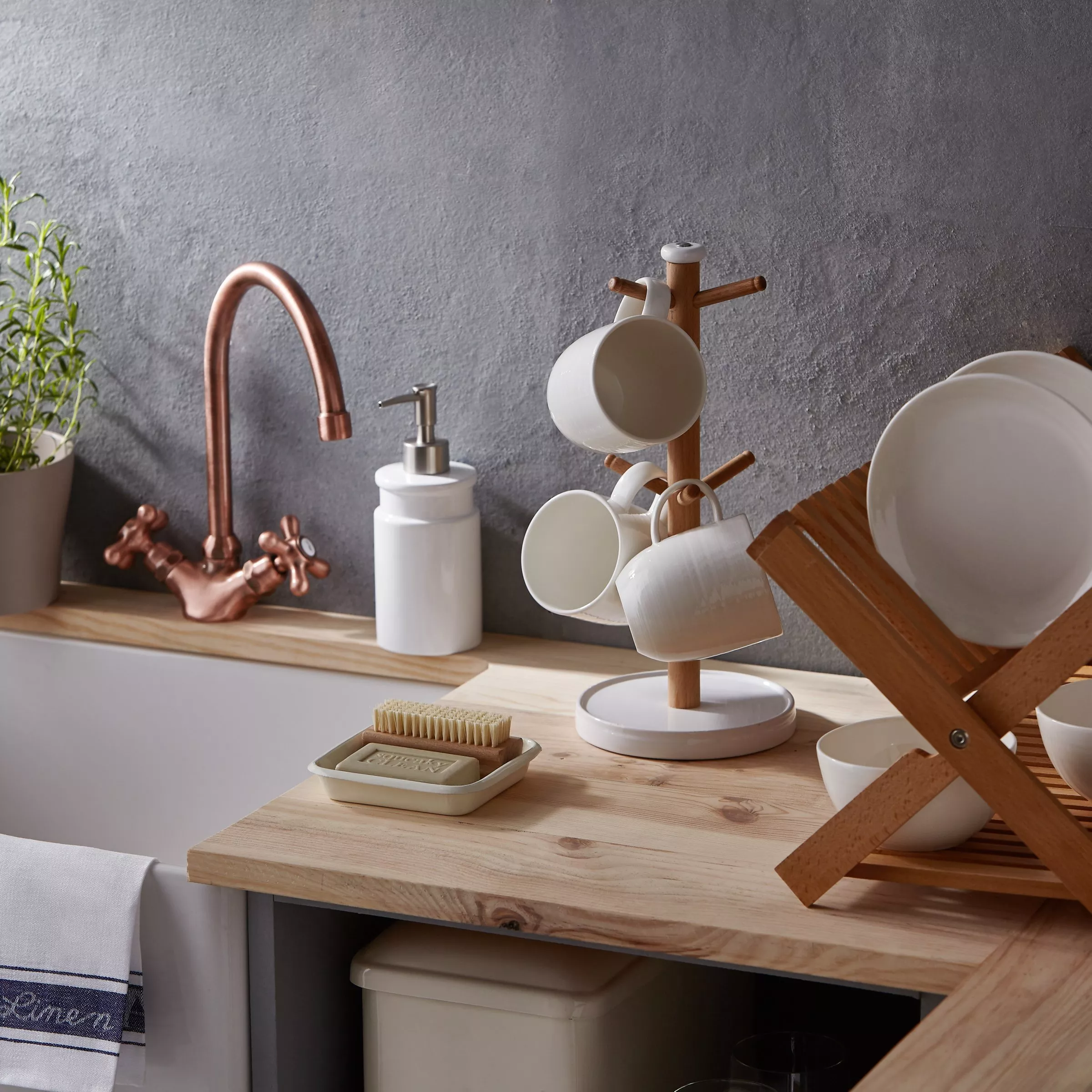 Modern kitchen sink with copper tap, wooden worktop, soap dispenser, mug tree and dish rack with plates