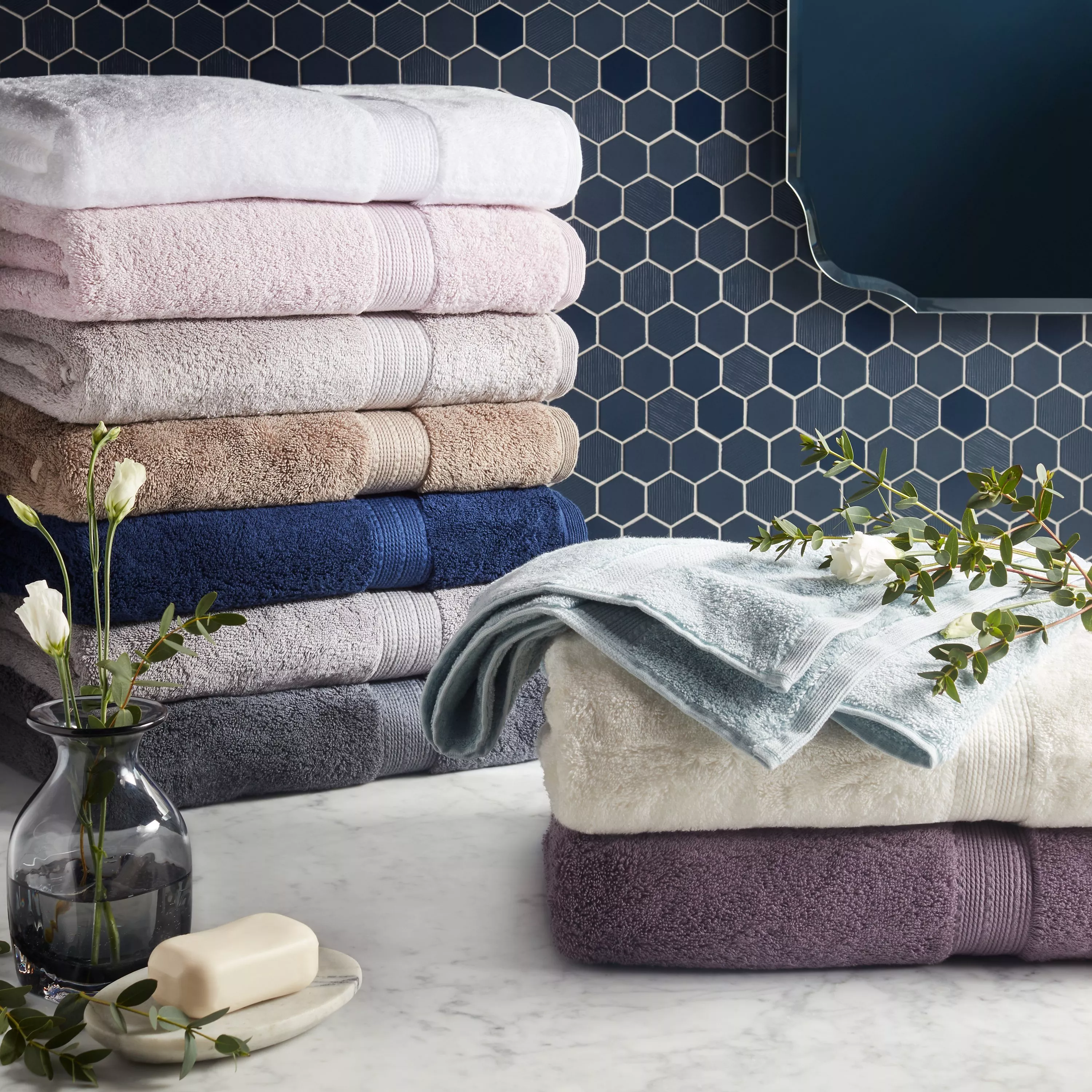 Stack of sage green cotton bath towels, including striped hand towel, neatly folded on white background