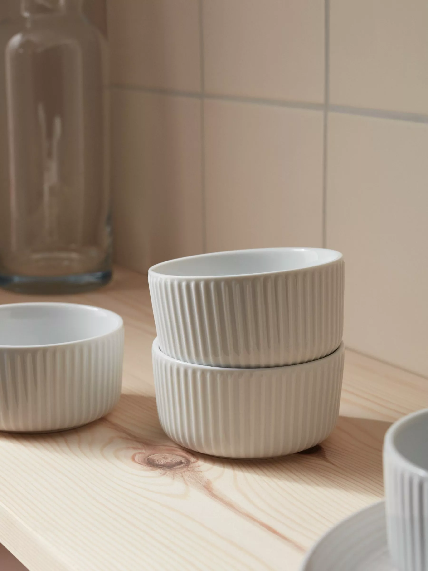 Blue ceramic casserole dish with handles on a white kitchen shelf beside stacked plates and glass tumblers
