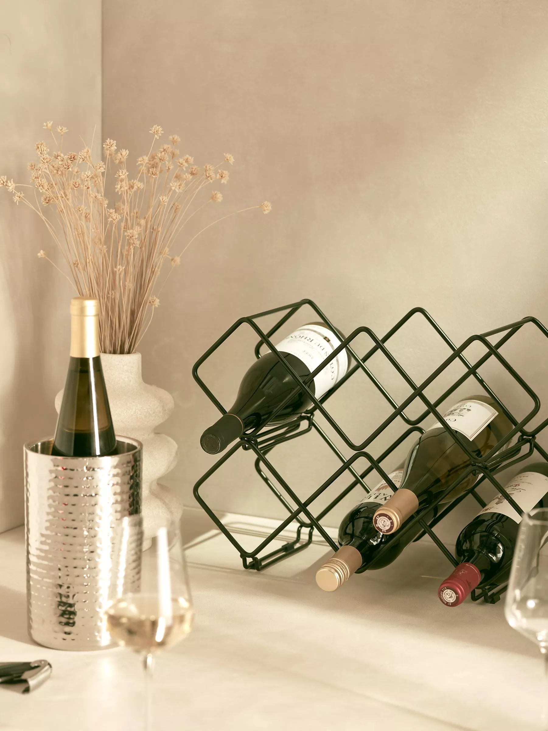 Stainless steel wine cooler bucket with ice and bottles, plus wine glass and corkscrew on table setting