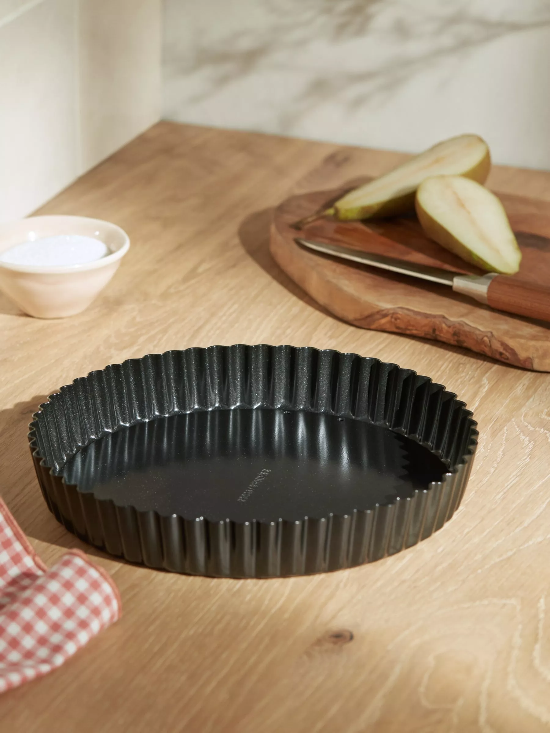 Flan tin on kitchen counter next to a sliced up pear