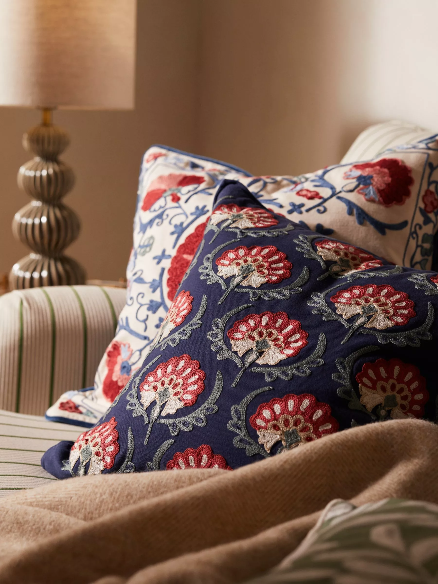 Cosy bedroom setting with a wooden headboard, patterned cushions, and a sleek gold lamp on a bedside table.