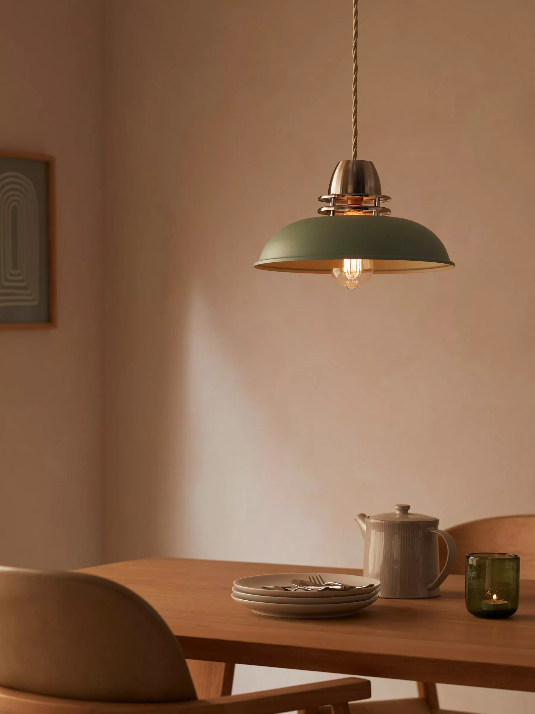 Green metal ceiling light hanging above a table with plates and cutlery