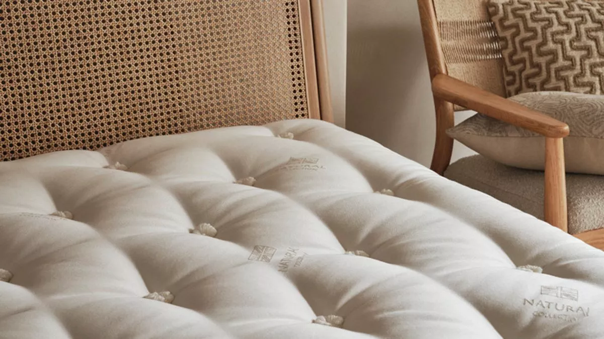 Luxurious tufted mattress with a woven headboard and a stylish chair with patterned cushions in a cosy setting.