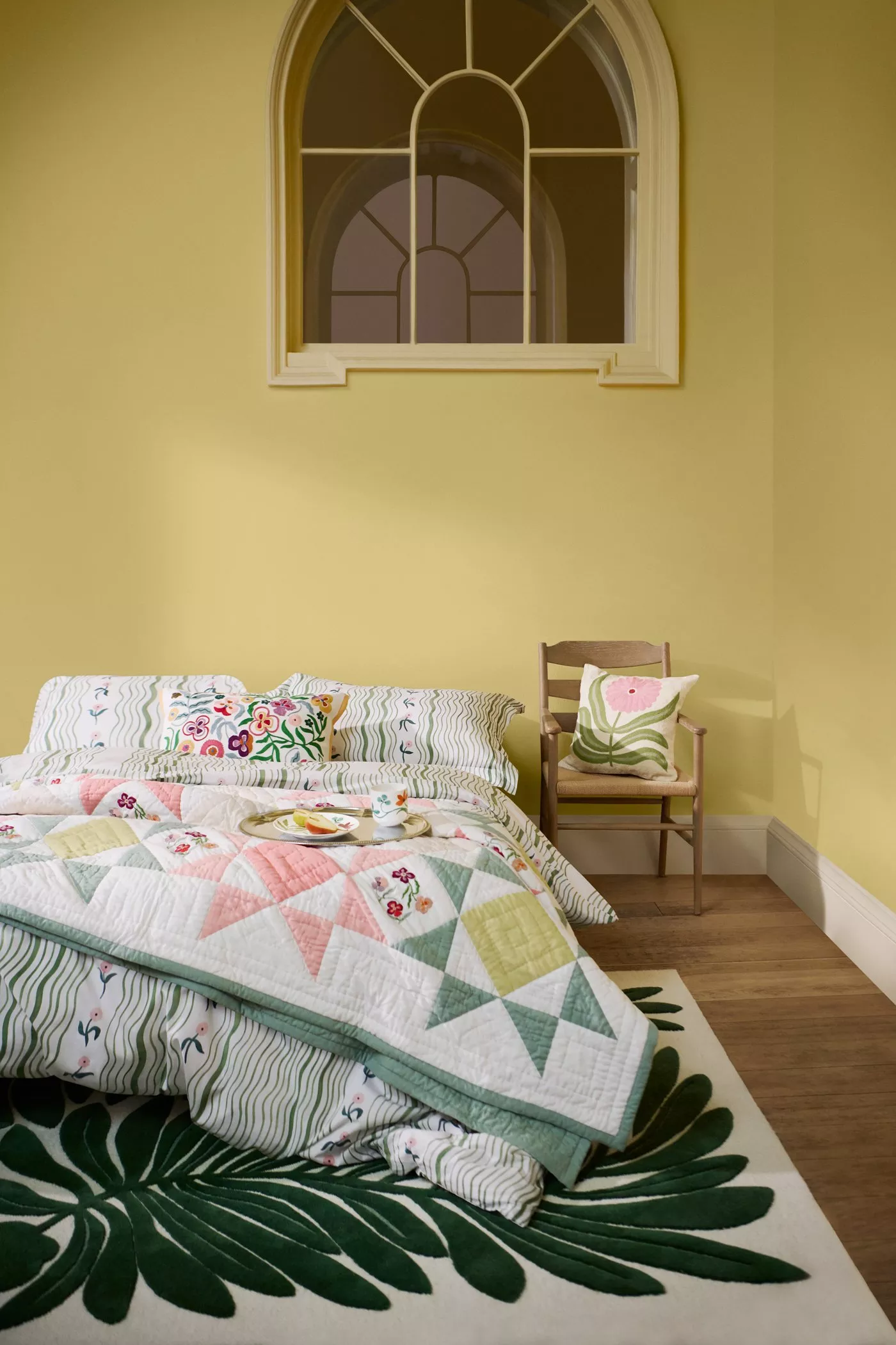 A stack of colourful bedding featuring floral and geometric patterns. Includes pillows and quilts on a wooden floor.