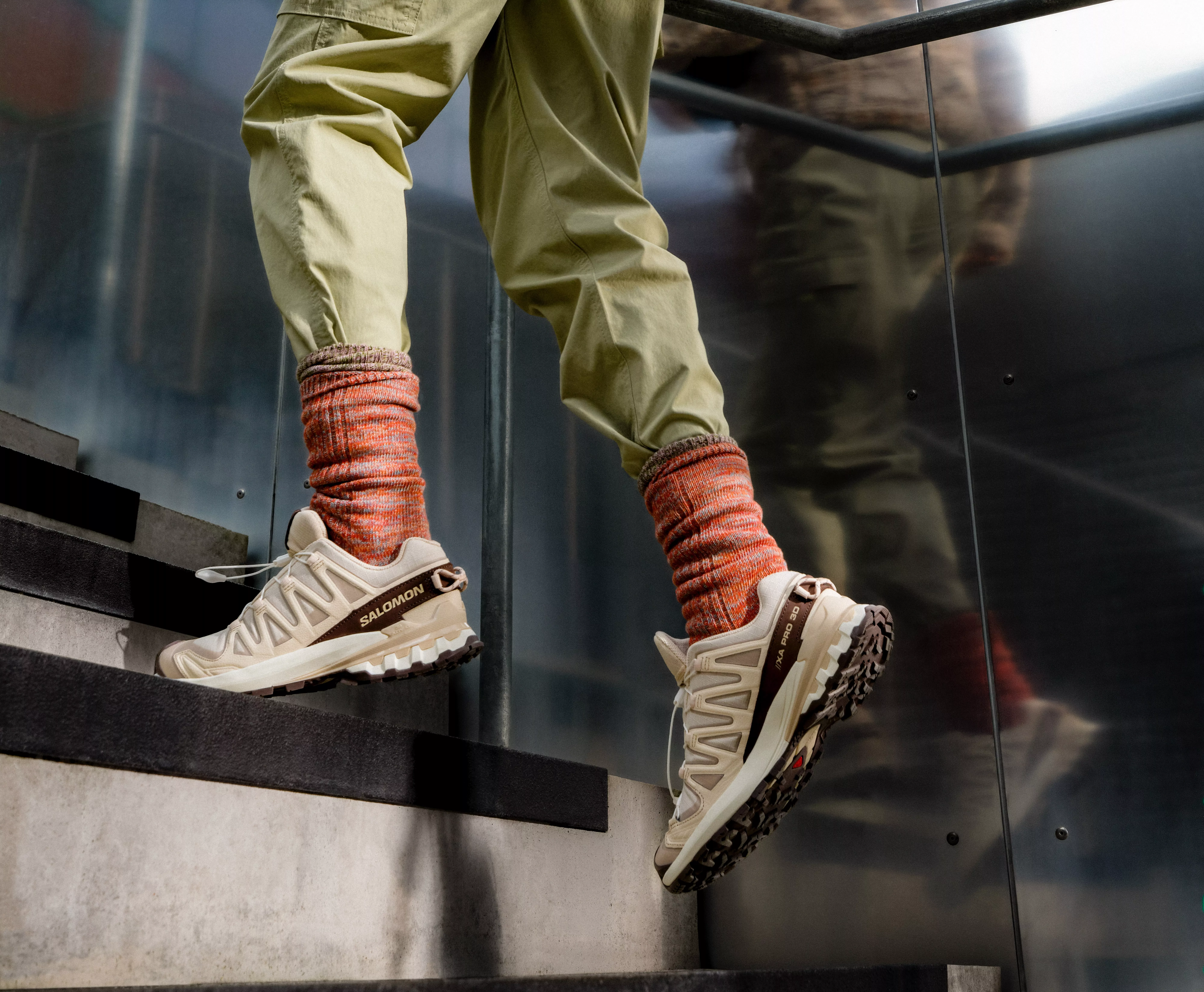 Close-up of person walking upstairs in Salomon trail trainers, orange socks and khaki trousers, urban setting
