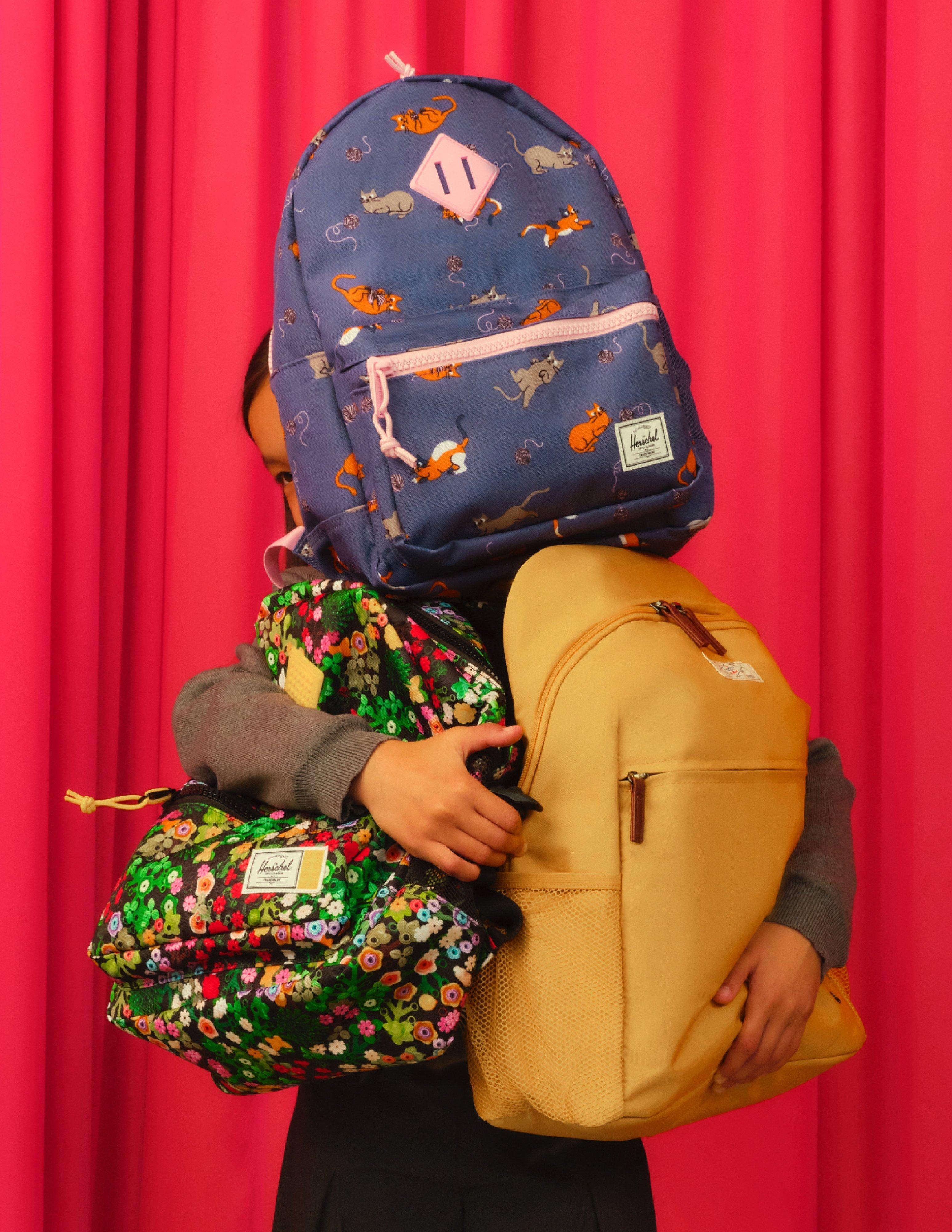 kid holding lots of backpacks covering her head