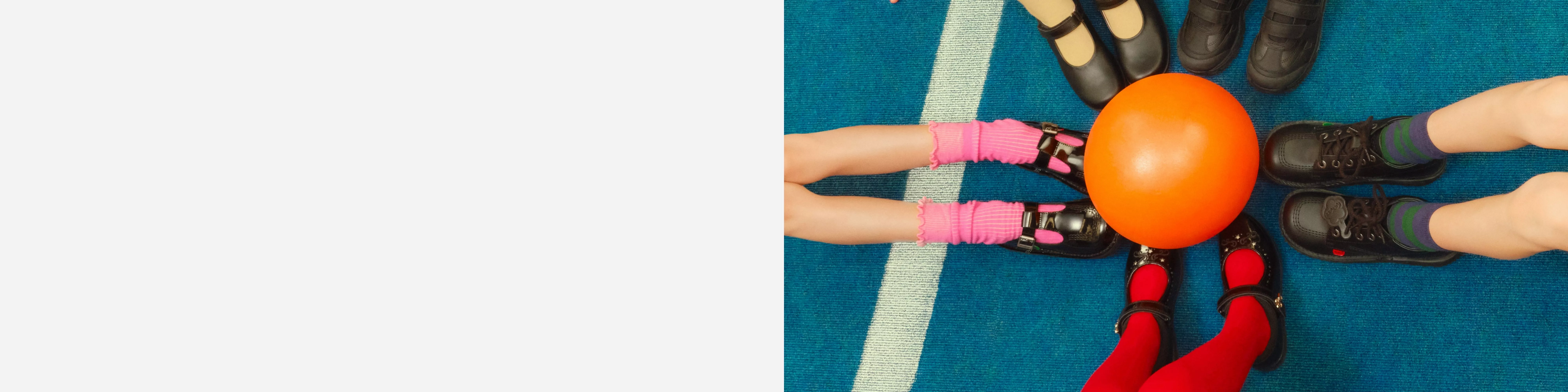 five kids feet wearing school shoes circled around an orange ball