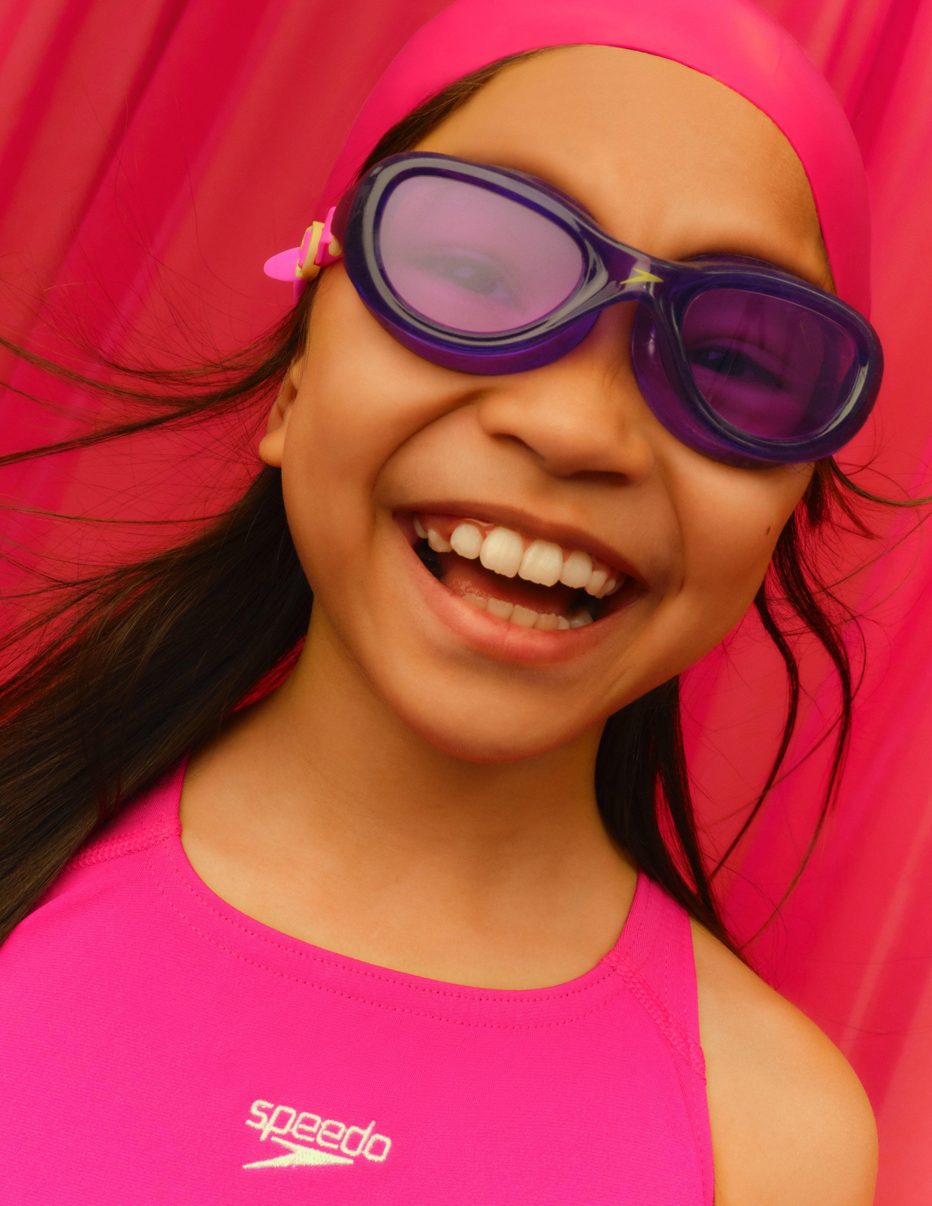 kid wearing swimming costume, googles and swimming hat looking happy