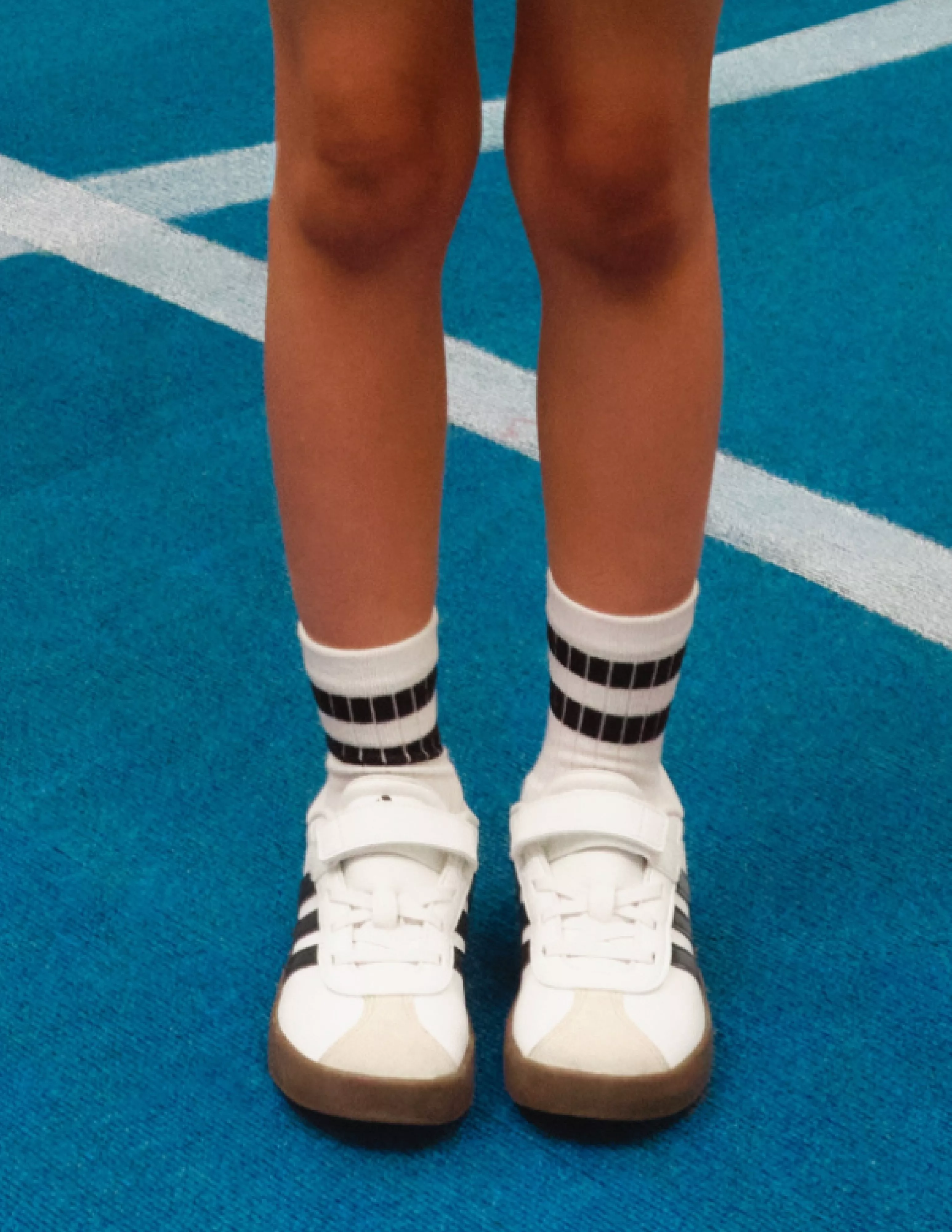 close up of a childs feet wearing white trainers on a blue court