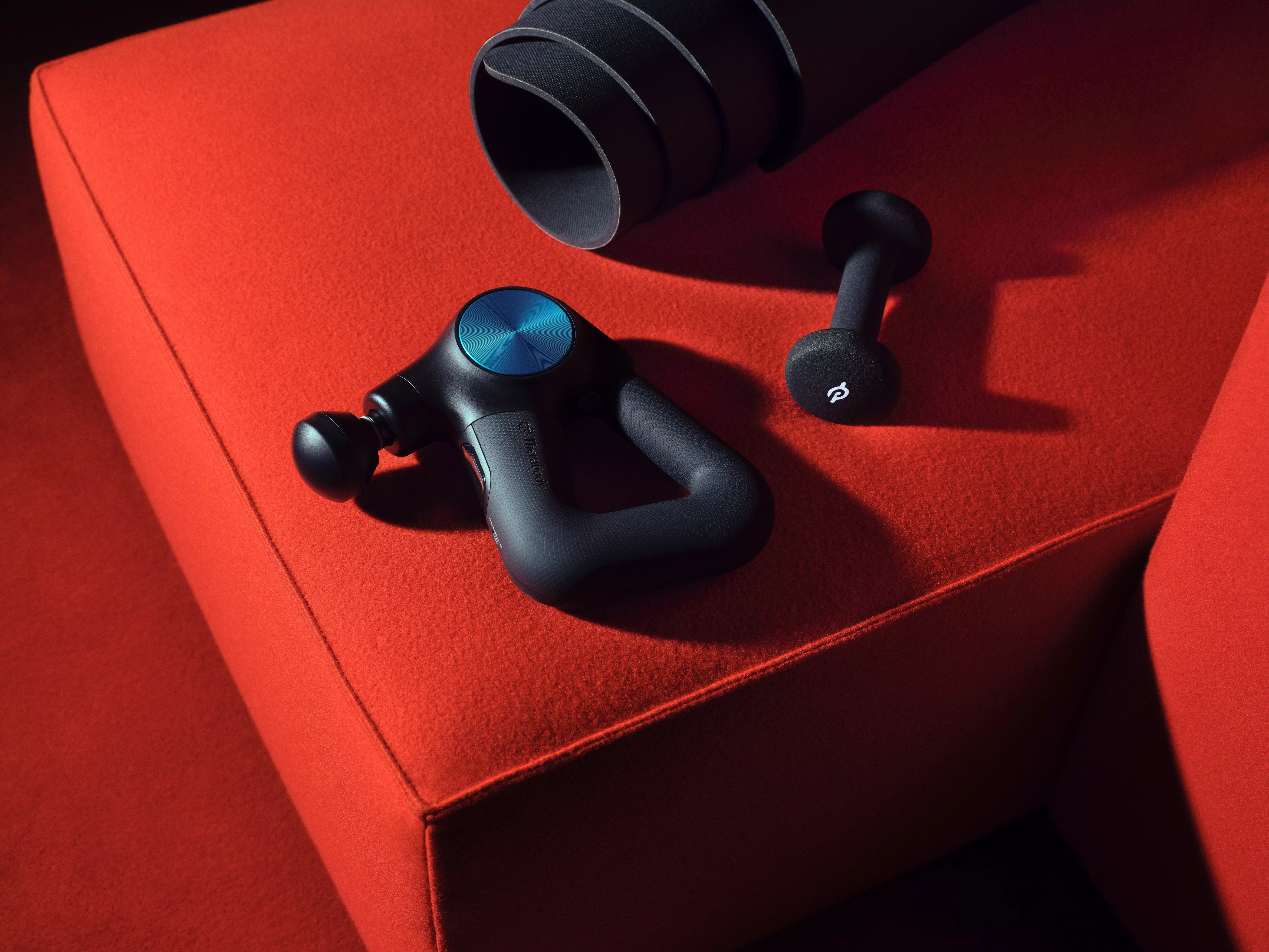 Percussion massage gun and mini handheld massager on red sofa, fitness recovery and muscle relief equipment