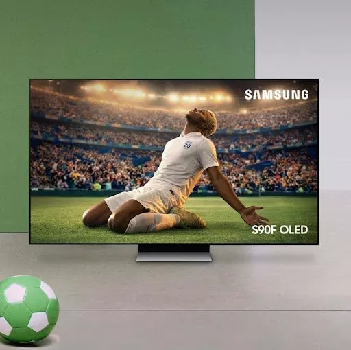 Samsung S90F OLED TV showing footballer celebrating on pitch in packed stadium, with ball in foreground