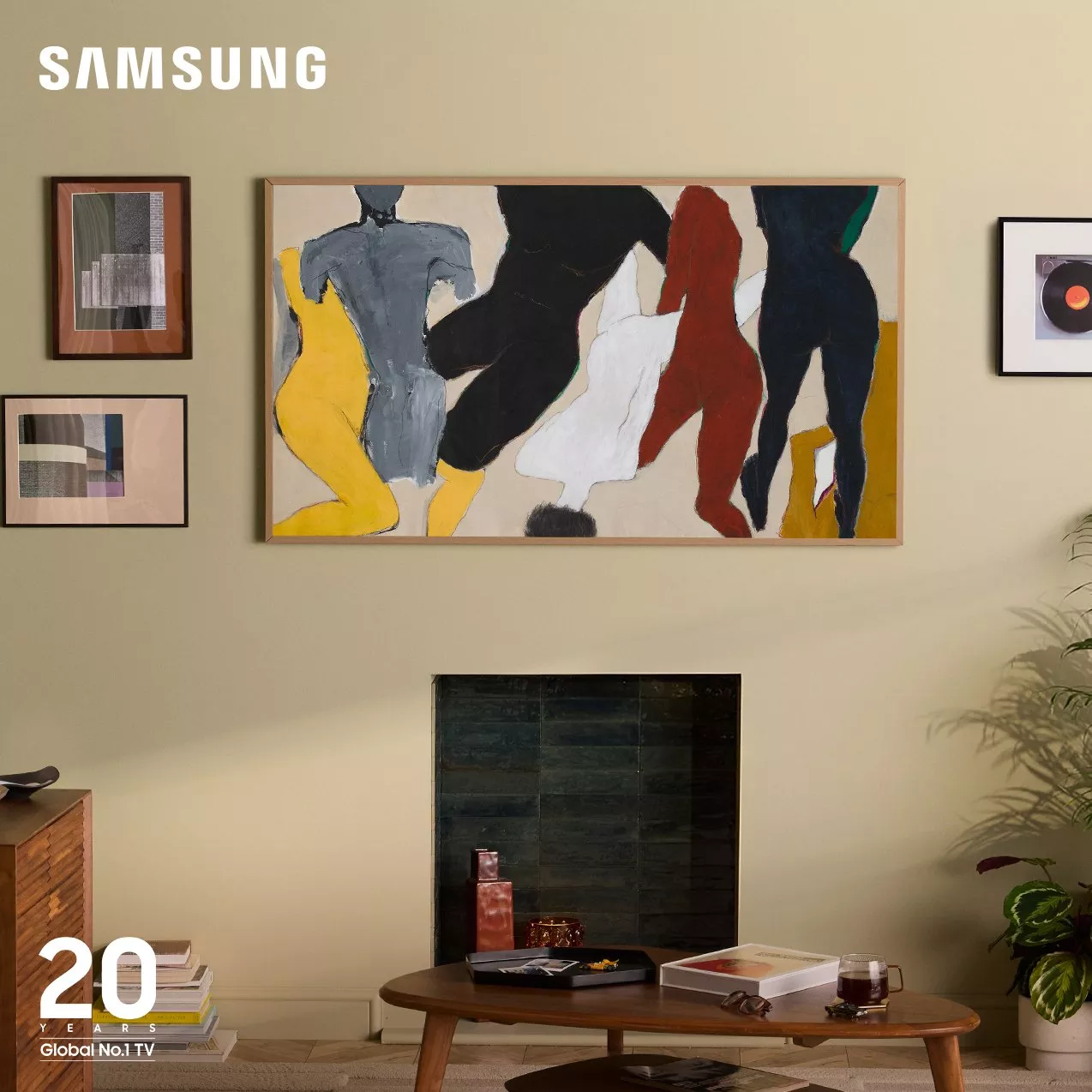 A Samsung The Frame TV mounted on a beige wall above a fireplace, displaying an abstract, stylized painting of multiple colorful figures in motion. The "Samsung" logo is in the top-left corner.