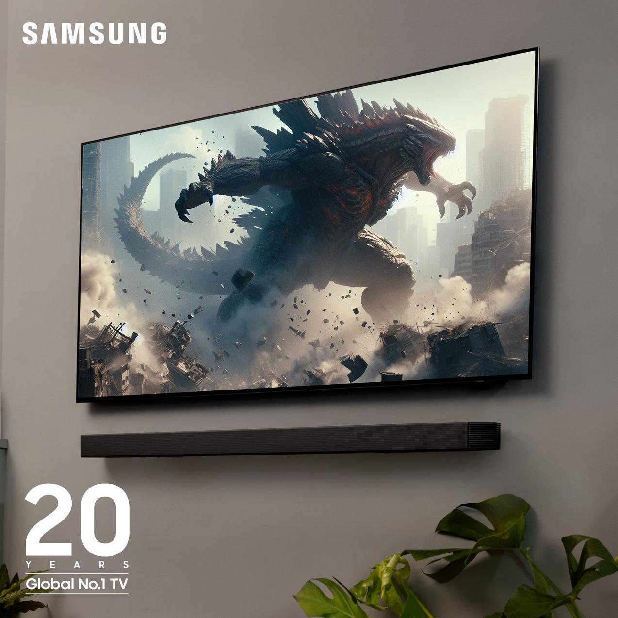 A wall-mounted Samsung TV displaying Godzilla, with a matching black soundbar below it. Text reads '20 Years Global No.1 TV'