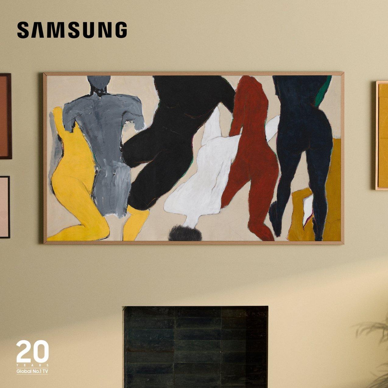 A Samsung The Frame TV mounted on a beige wall above a fireplace, displaying an abstract, stylised painting of multiple colorful figures in motion. The "Samsung" logo is in the top-left corner.