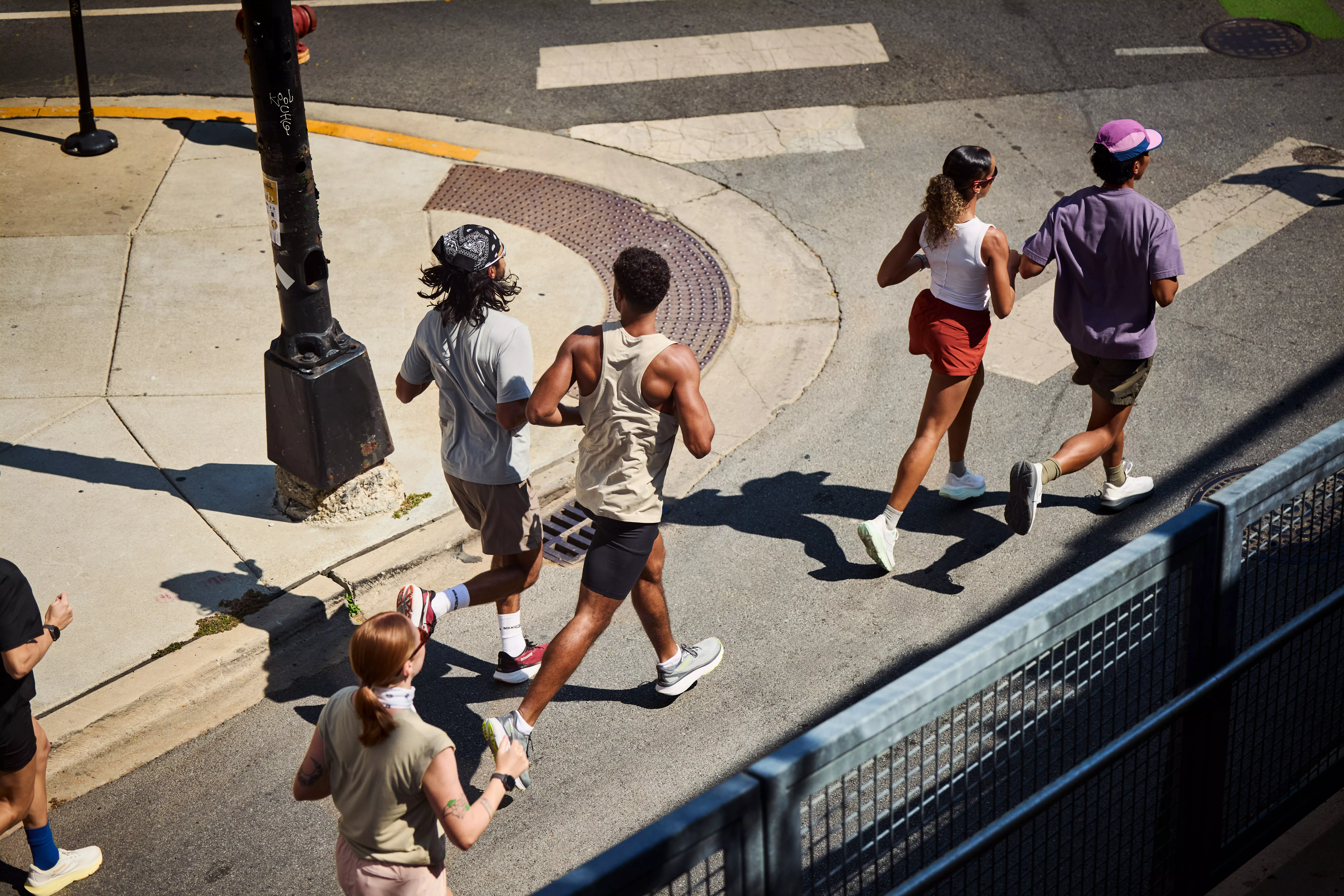 Group of runners jogging across a city street junction on a sunny day, seen from above at a road crossing