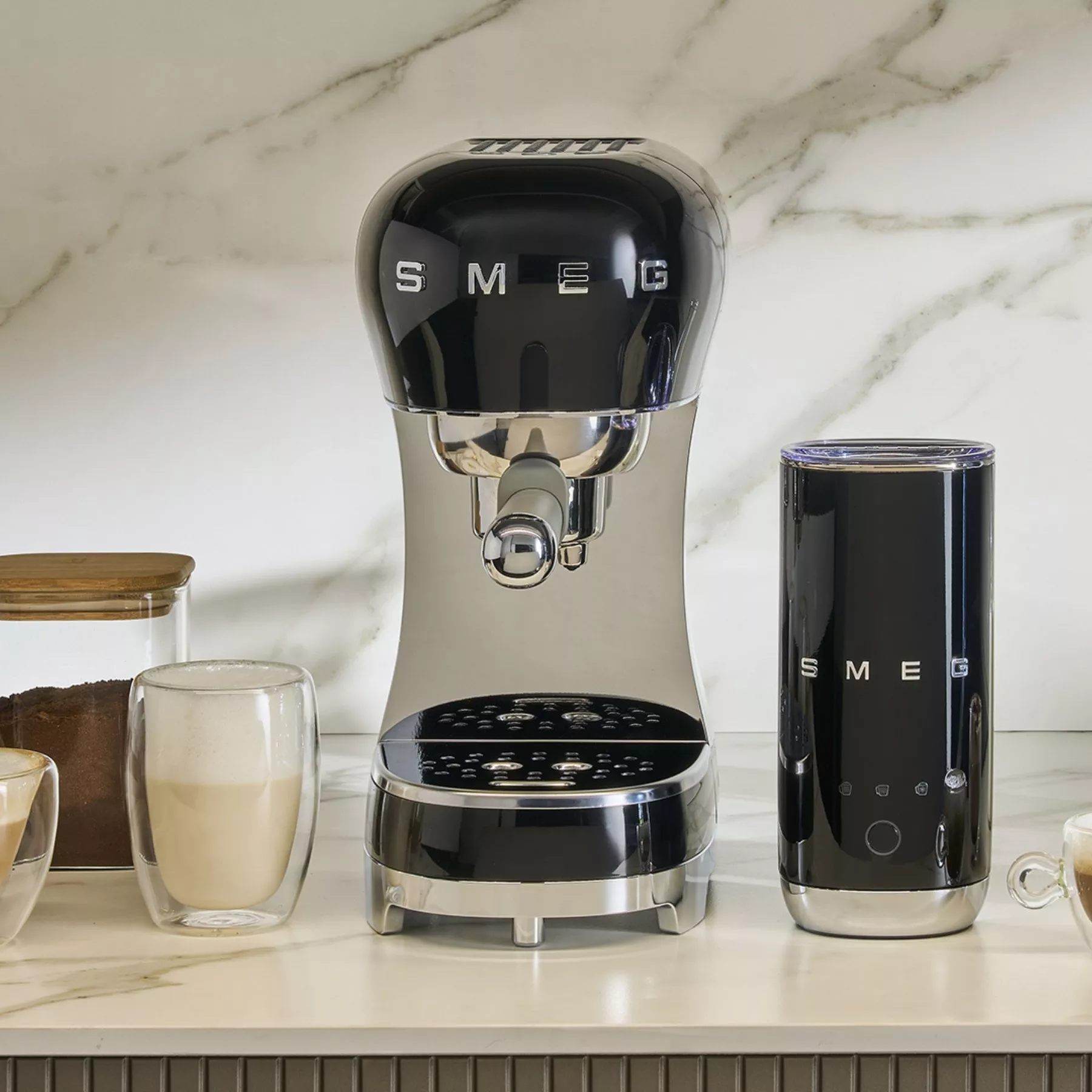 Black SMEG espresso machine and matching milk frother on marble kitchen worktop with latte glass and coffee jar