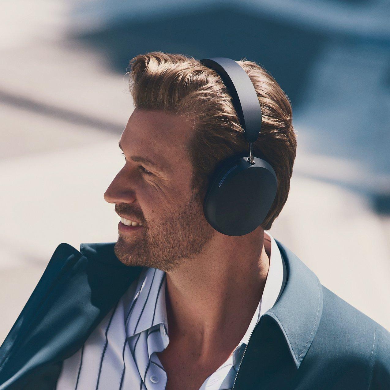 Profile shot of a man smiling outdoors while wearing black over-ear wireless Sonos headphones.
