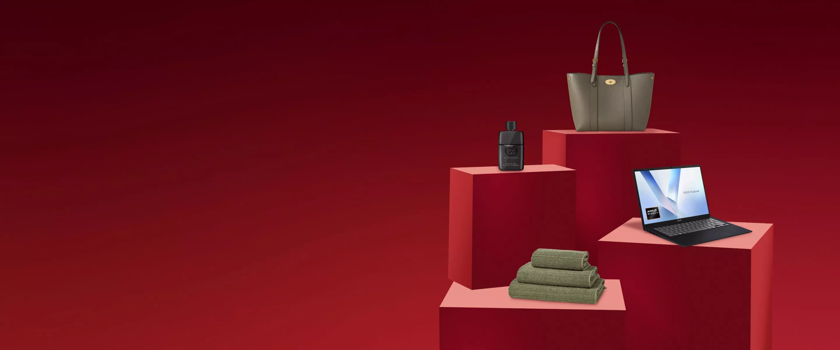 Grey leather tote bag, perfume bottle, laptop and folded towels on red podiums against a dark red backdrop