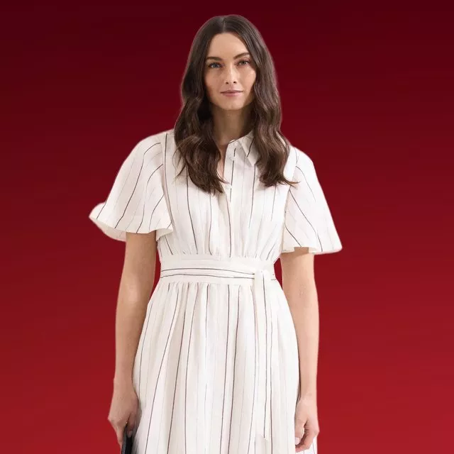 Woman modelling a white striped midi dress with flutter sleeves and waist belt, studio fashion shot on red background