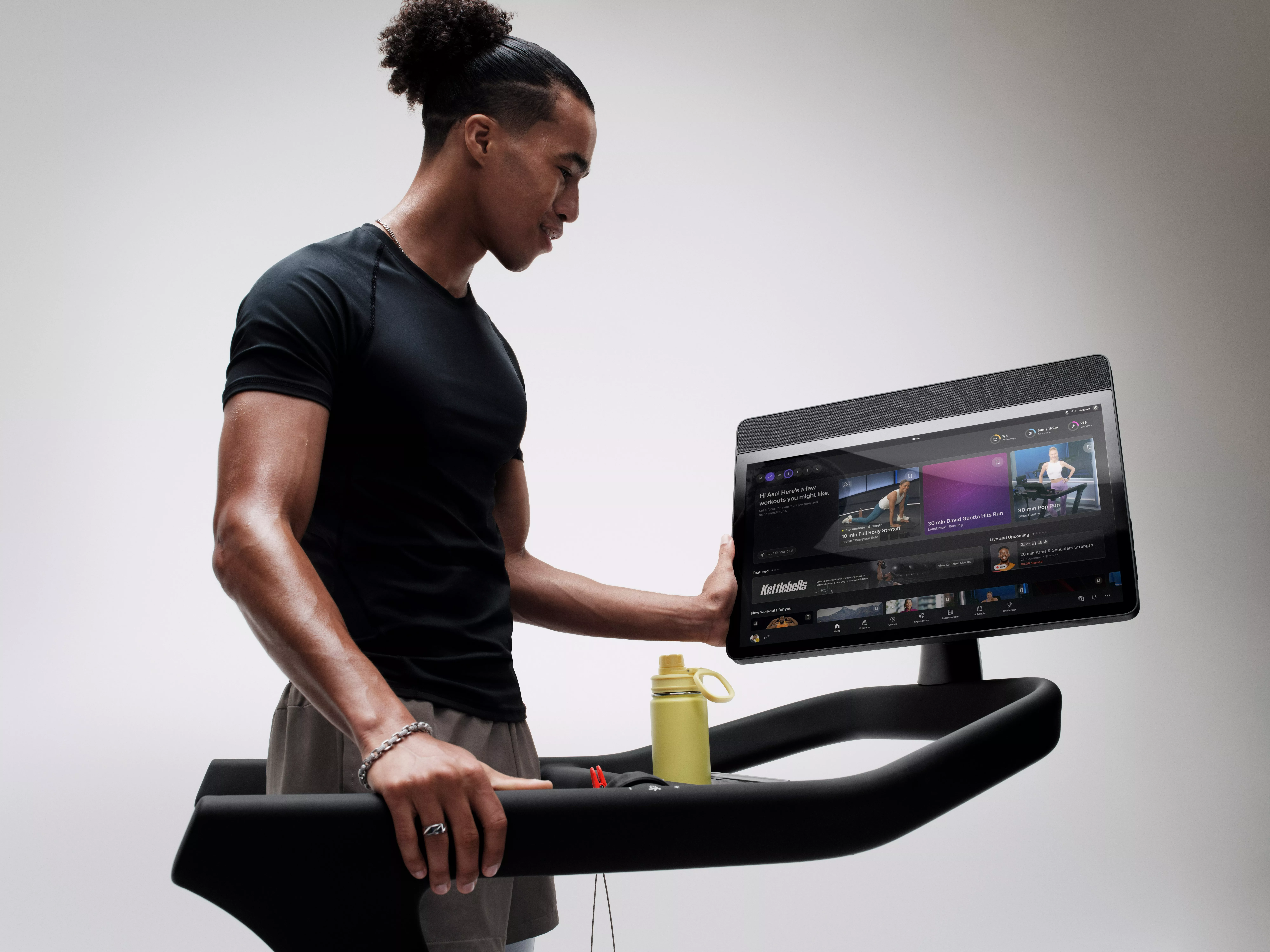 Man using smart treadmill touchscreen to choose guided fitness workouts, with water bottle on console in gym