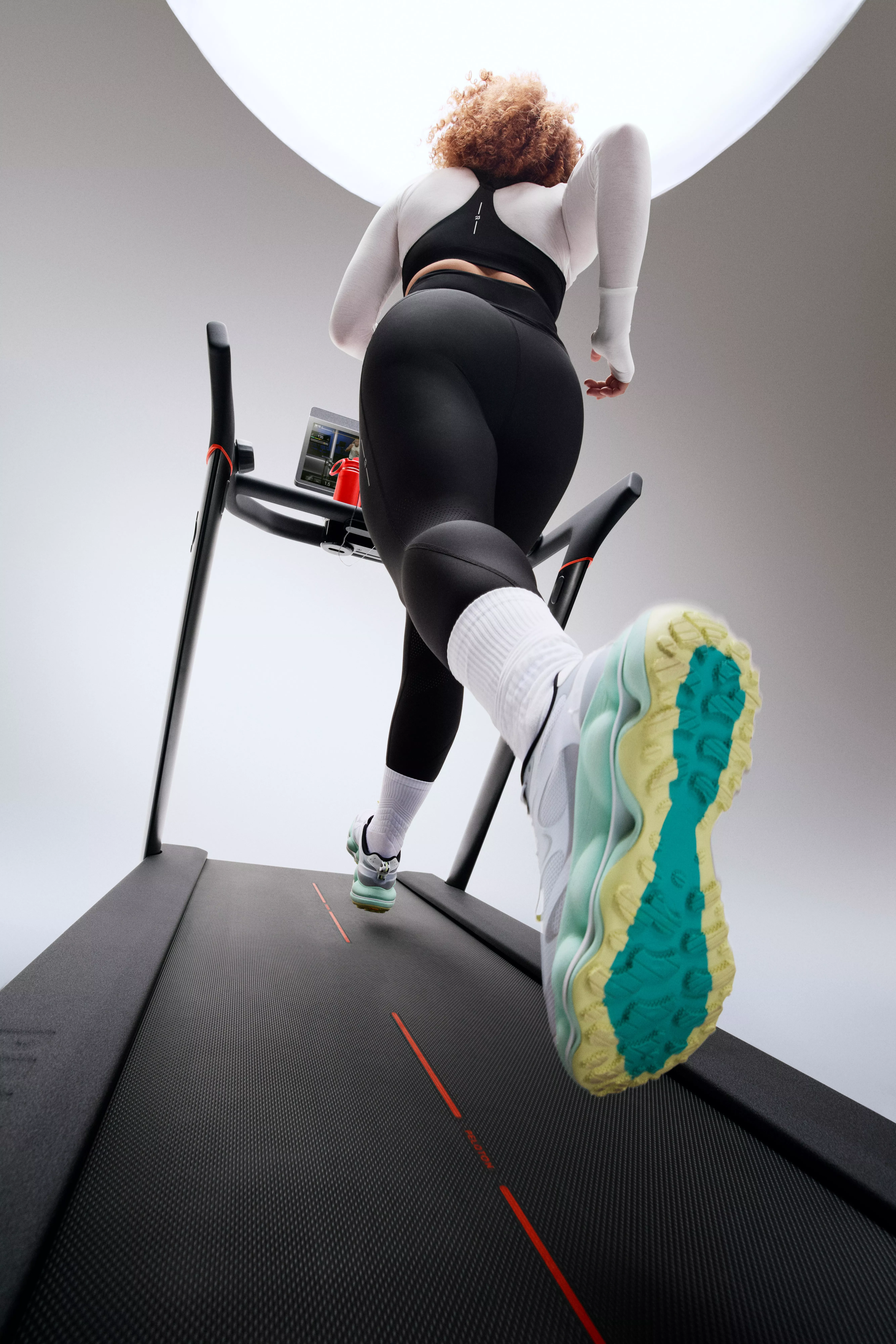 Low-angle view of woman running on treadmill in modern gym, wearing black leggings and trainers, cardio workout
