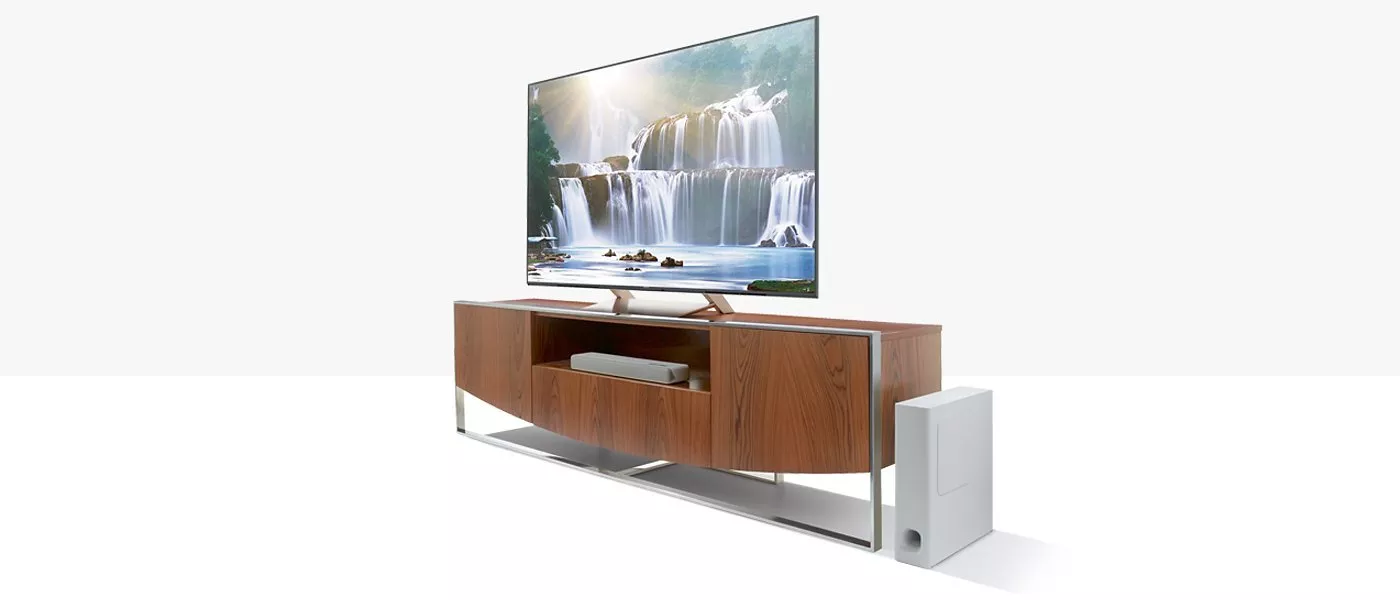 Modern entertainment setup with a sleek wooden TV stand, large flat-screen displaying a waterfall, and a white speaker.