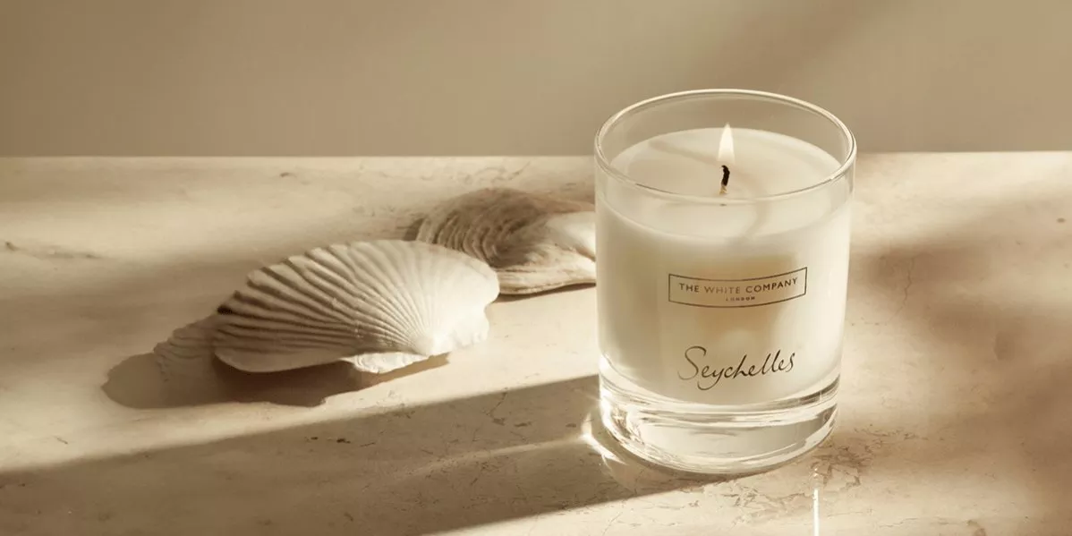 This is banner for The White Company with the Seychelles candle surrounded by shells.