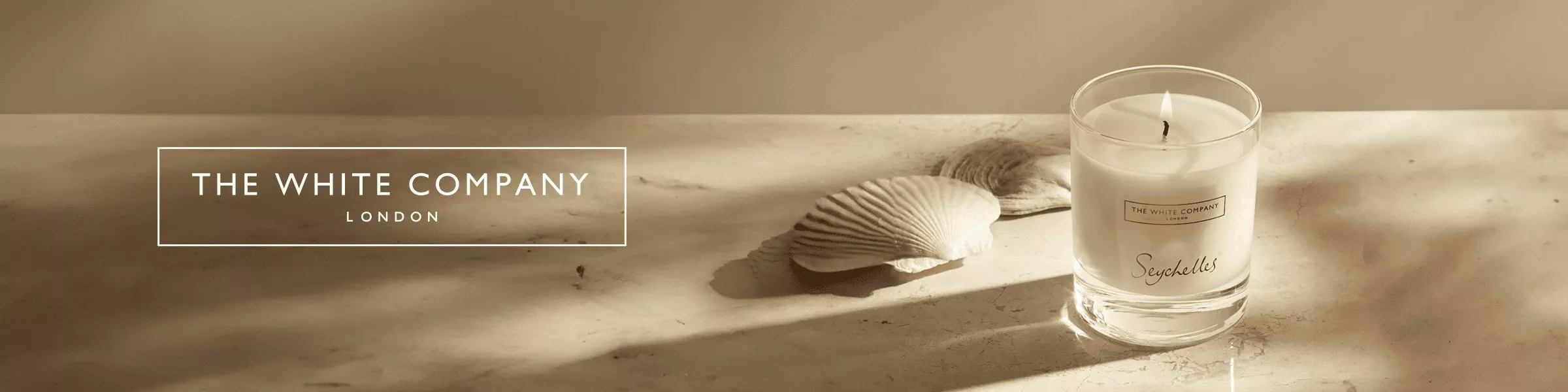 The White Company London Seychelles scented candle in glass jar on marble surface with seashells in soft light