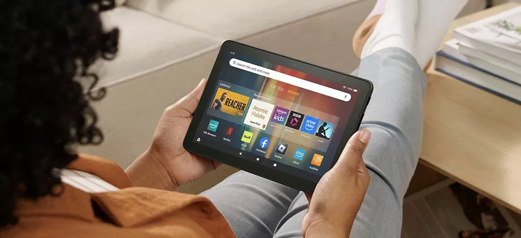 Person relaxing on sofa holding a tablet showing a streaming home screen, browsing films and TV apps