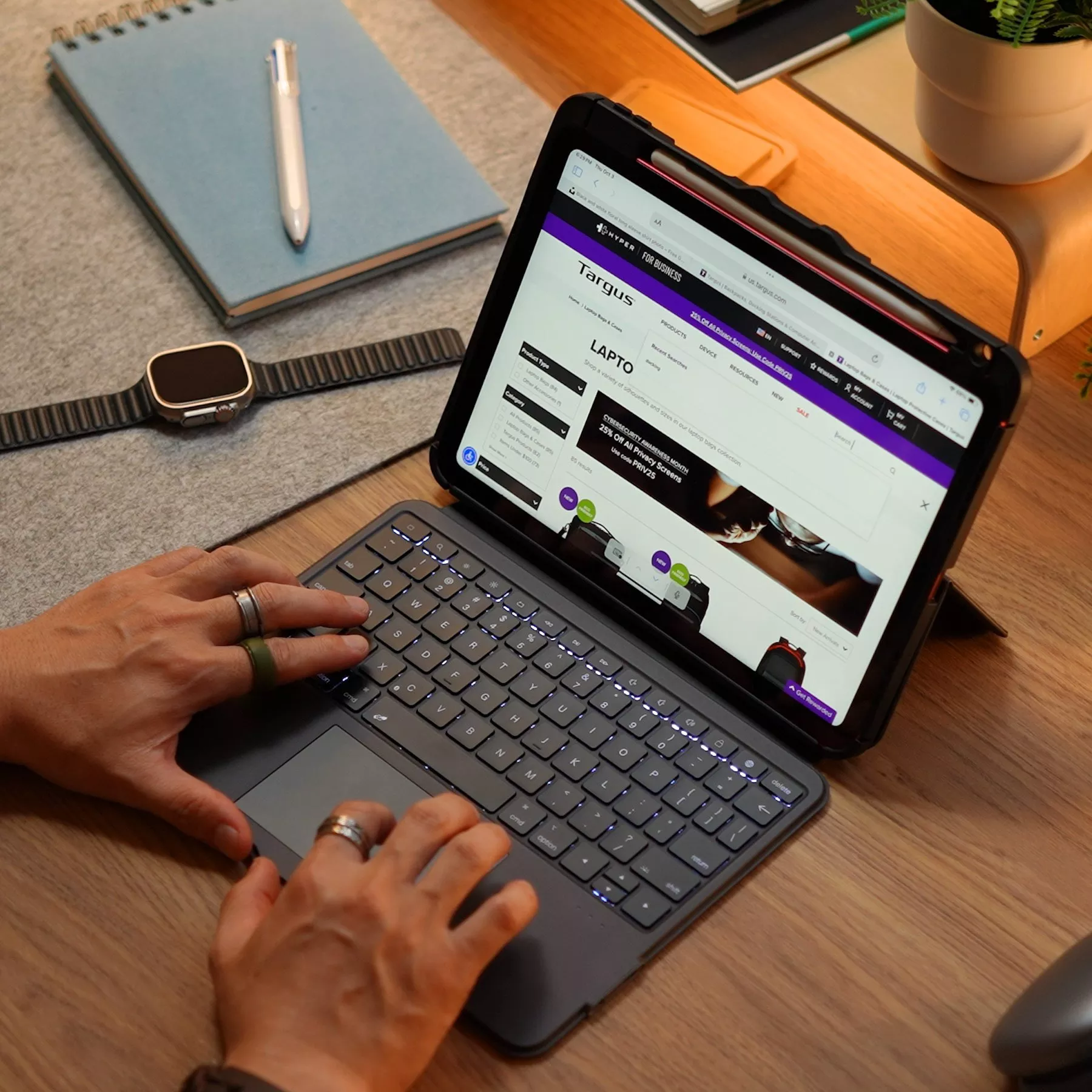 Hands typing on iPad with Bluetooth keyboard on wooden desk, smartwatch, notebook and pen in home office setup
