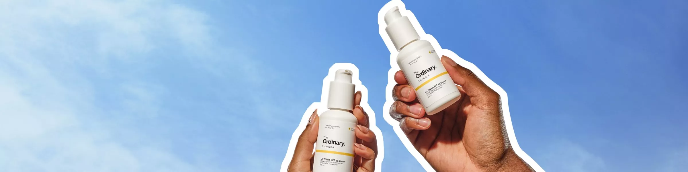 Hands holding The Ordinary SPF 45 sunscreen bottles against blue sky background, minimalist skincare product photo