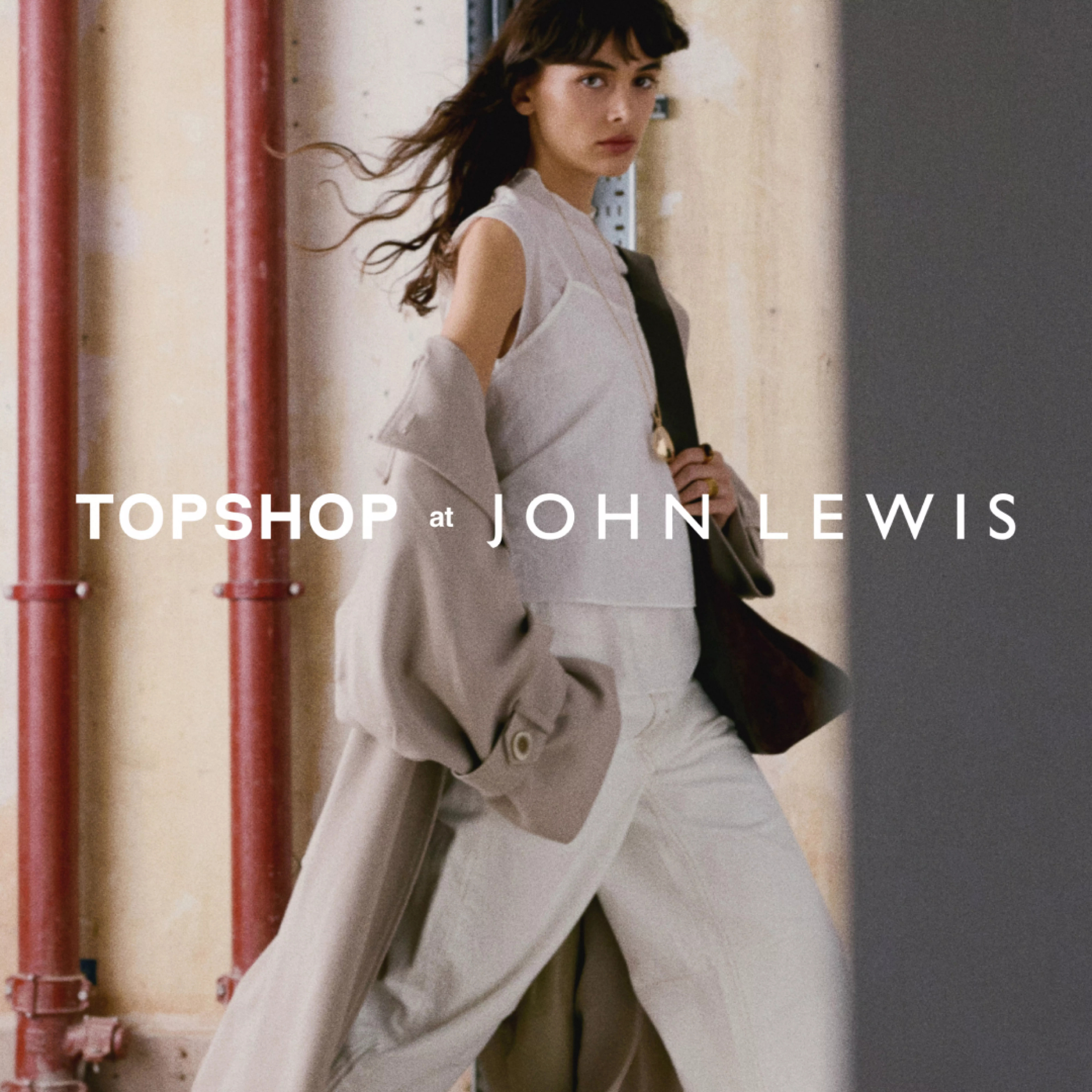 Woman in a dark, striped dress leans against a textured wall in a vintage room with a fireplace and wooden door.