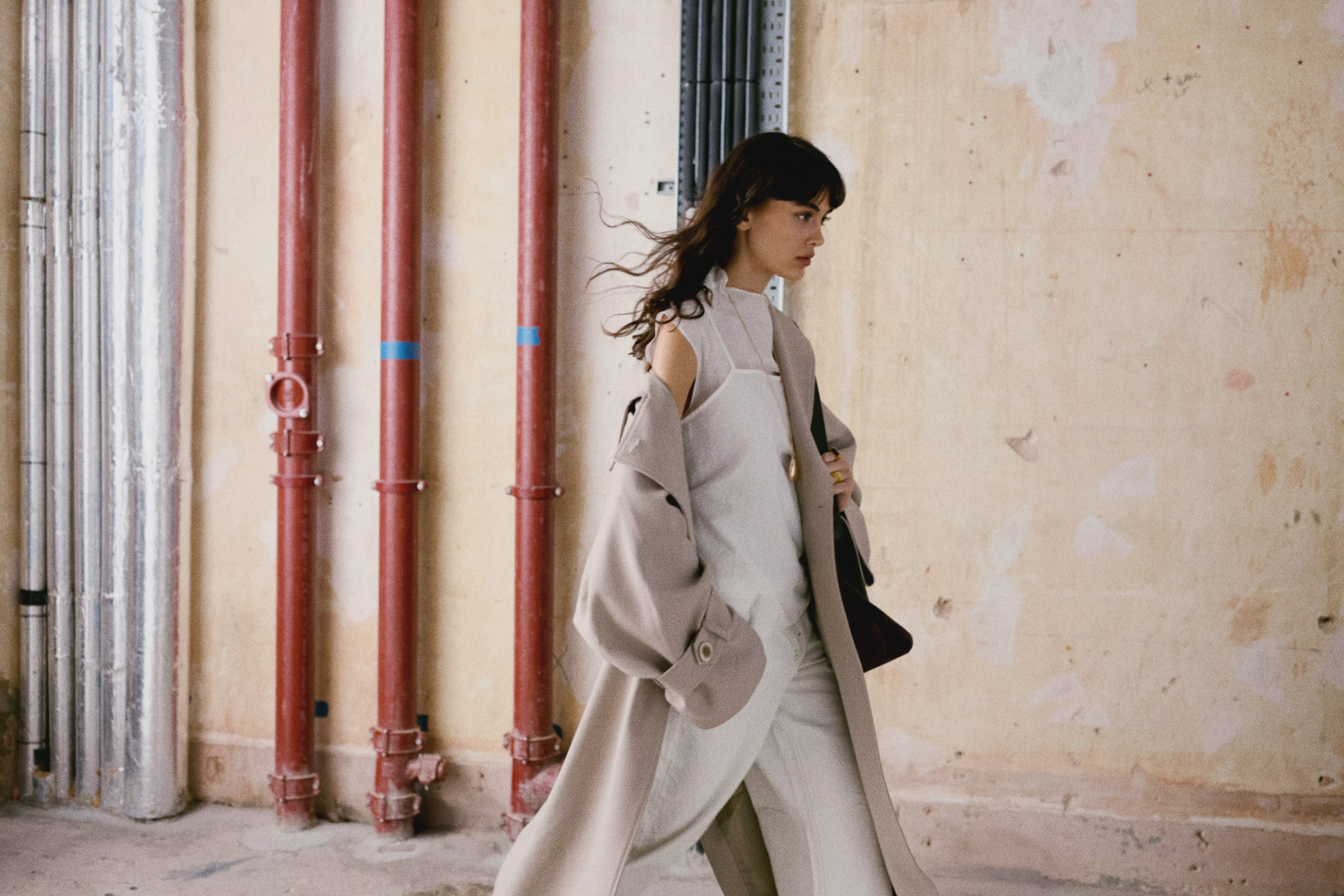 Woman in a dark, striped dress leans against a wall in a softly lit room, exuding a calm and elegant vibe.