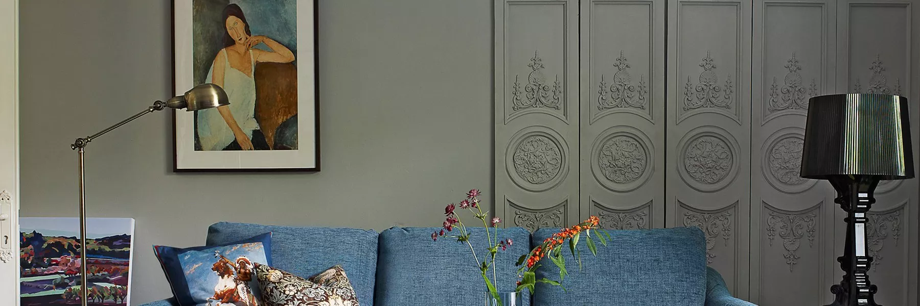 Stylish living room with blue sofa, framed art, brass floor lamp and grey panelled wall décor background