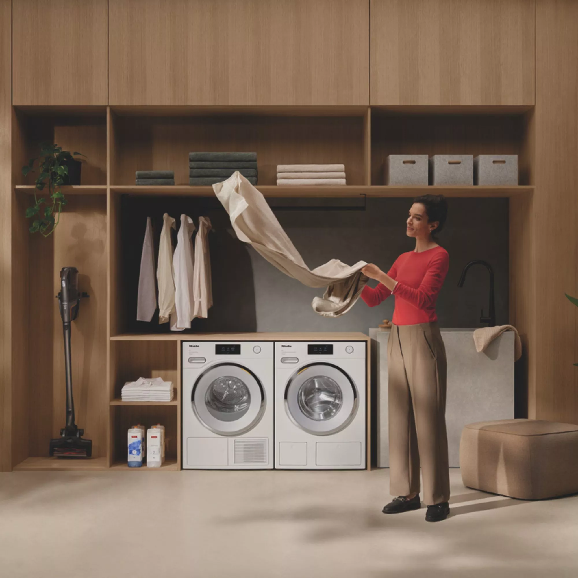 Modern laundry room with built-in washer dryer, organised wooden storage and person folding fresh clothes
