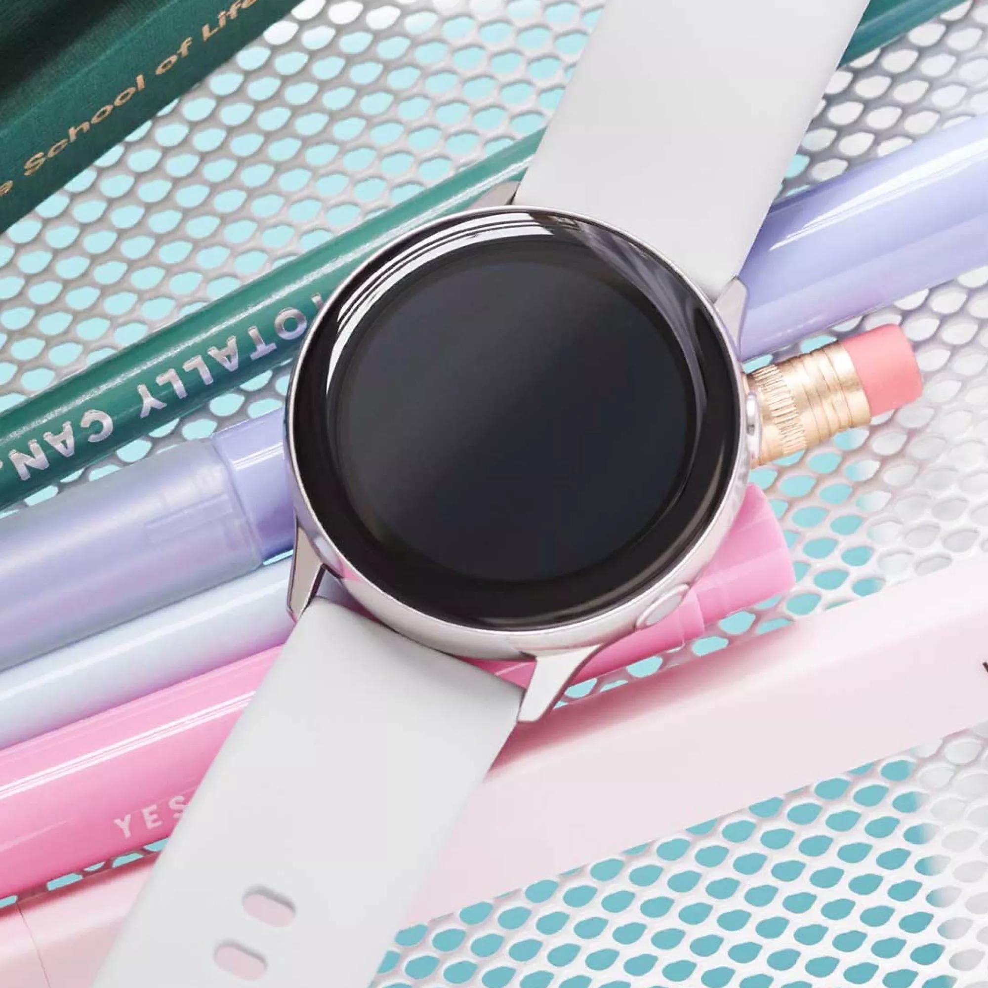 White smartwatch on pastel pens and pencil over a mesh desk, minimal tech flat lay for school stationery shopping