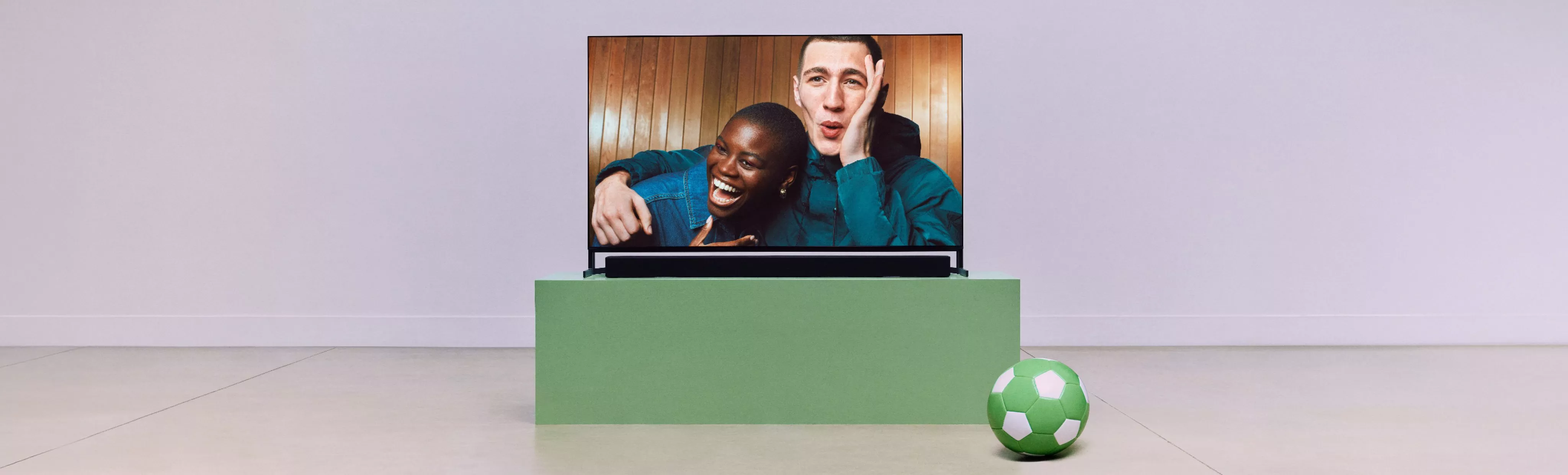 Poster reading “Meet the next-gen TVs” above a wall-mounted TV and soundbar in a living room setup with snacks