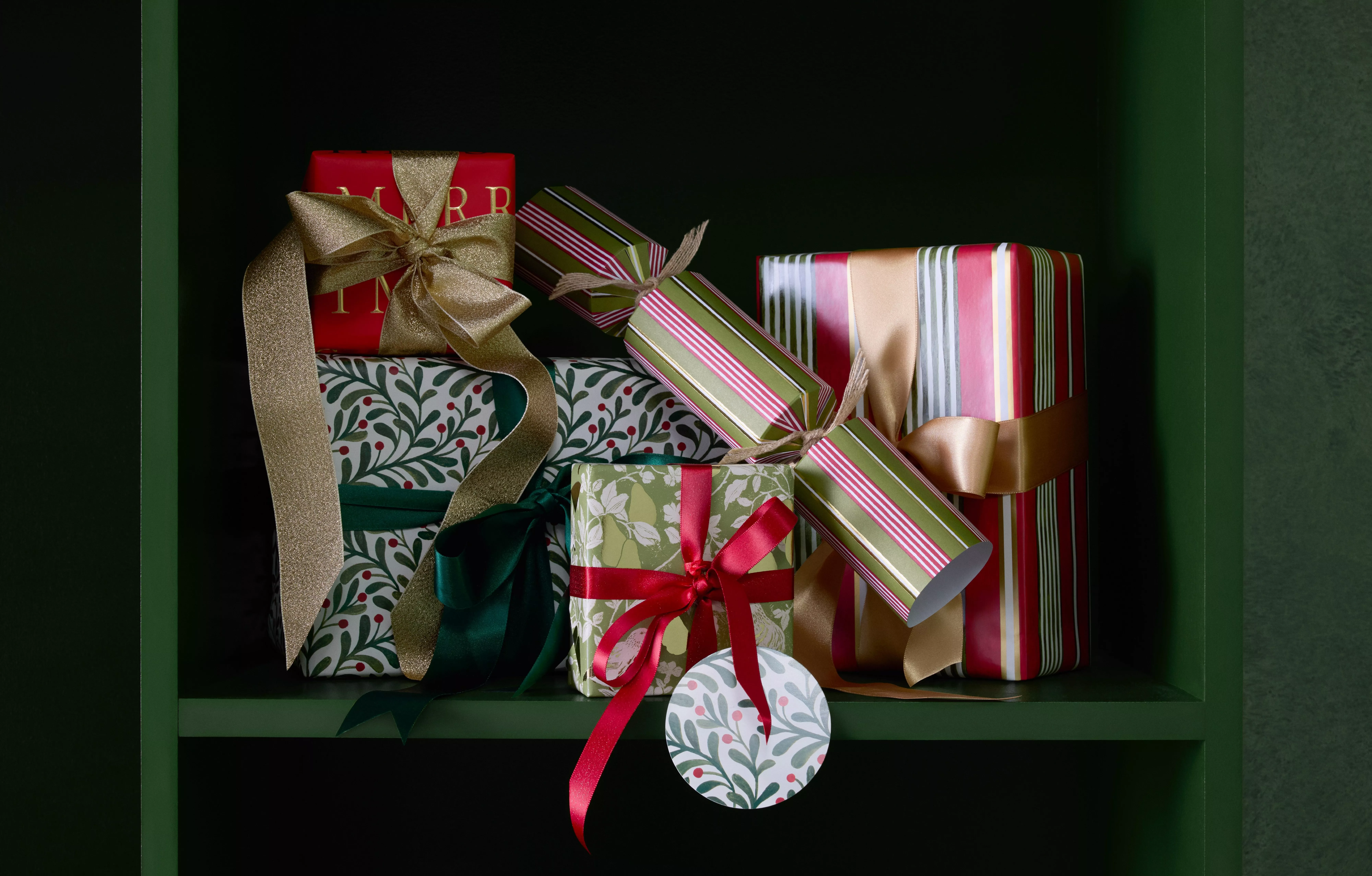 Christmas gift boxes with festive wrapping, gold and red ribbons, and crackers arranged on a green shelf