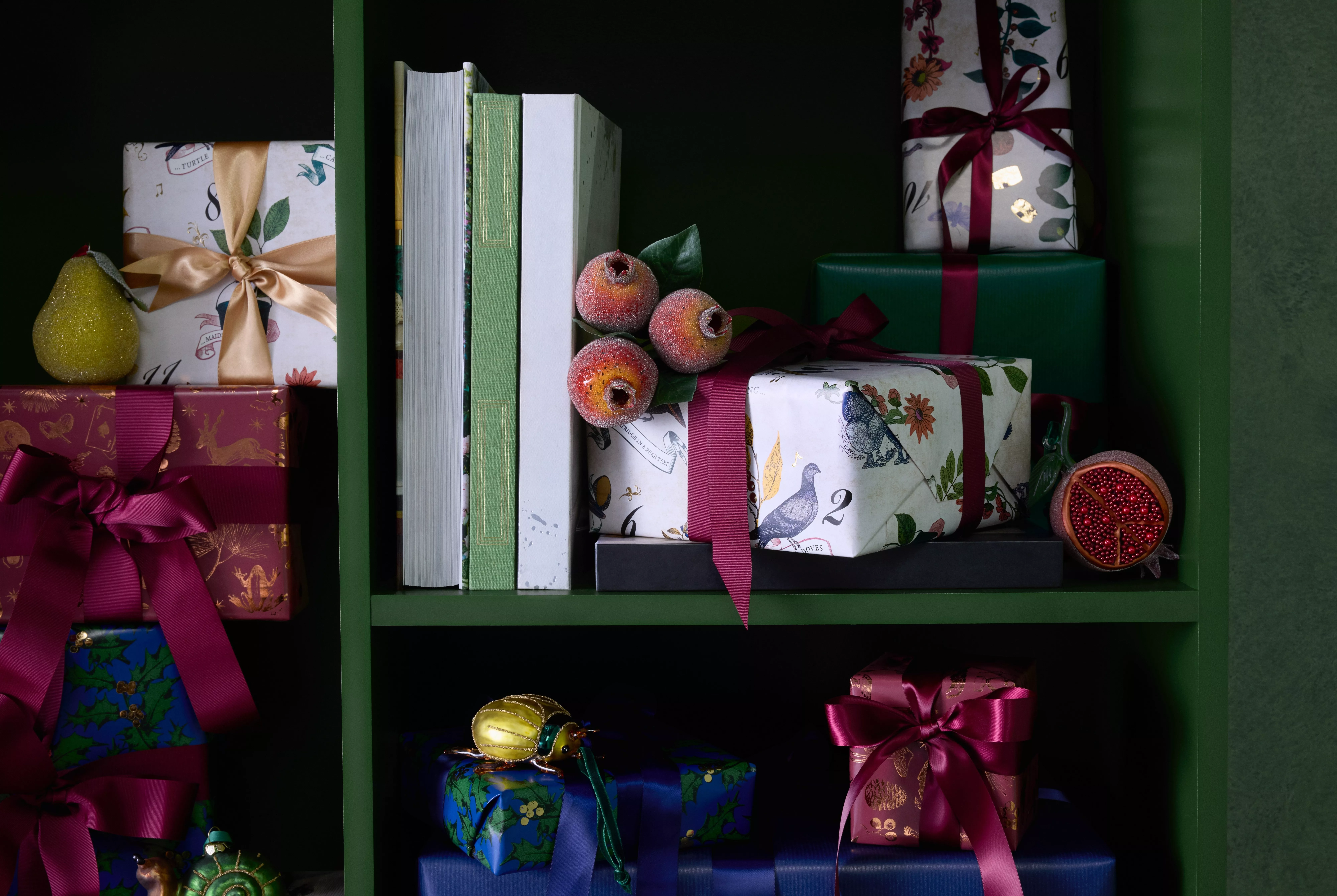 Festive wrapped Christmas gifts on green shelving with books, pears, pomegranate and ribbons in rich colours