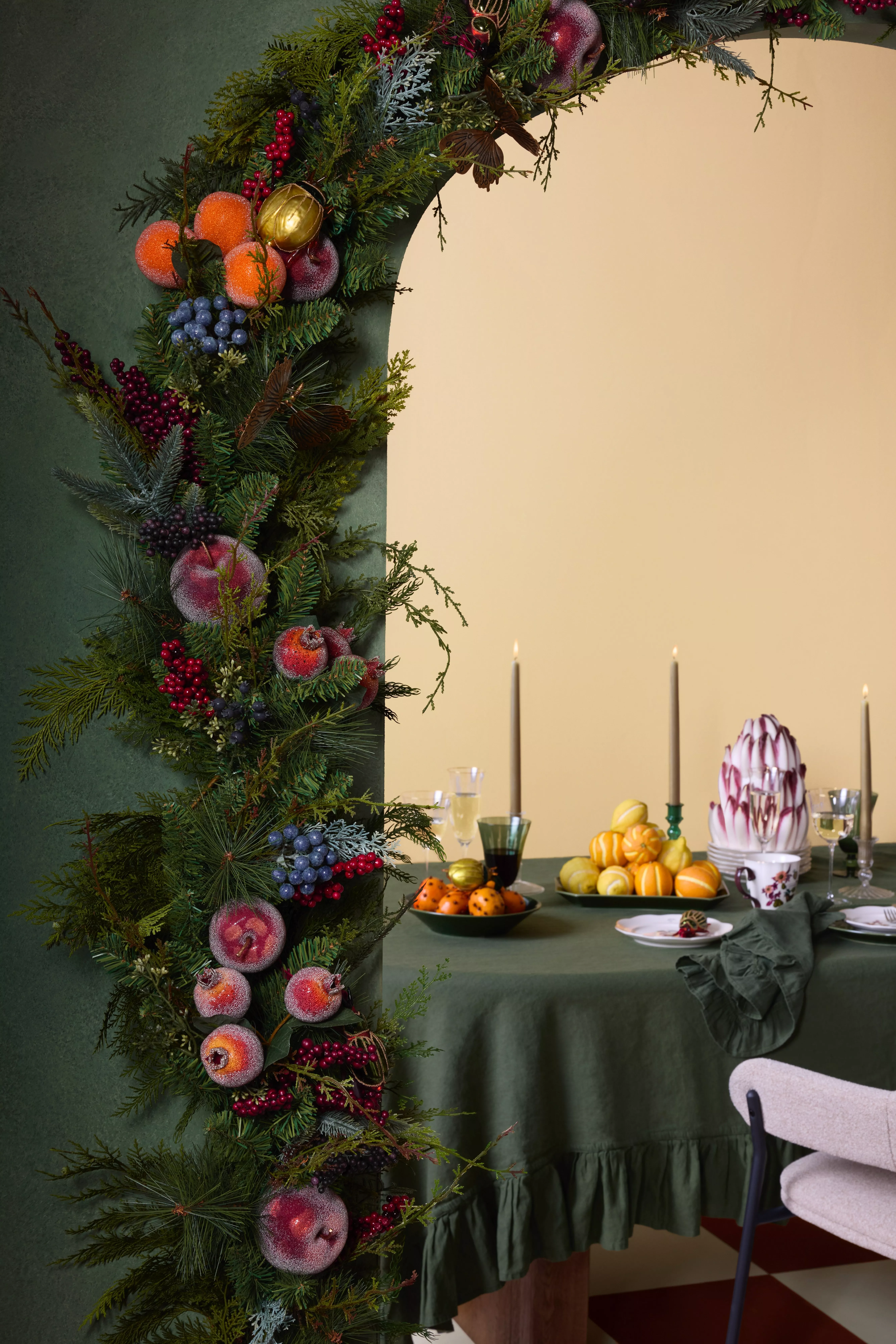 Festive Christmas garland with frosted fruit and berries framing dining table with candles and citrus centrepiece
