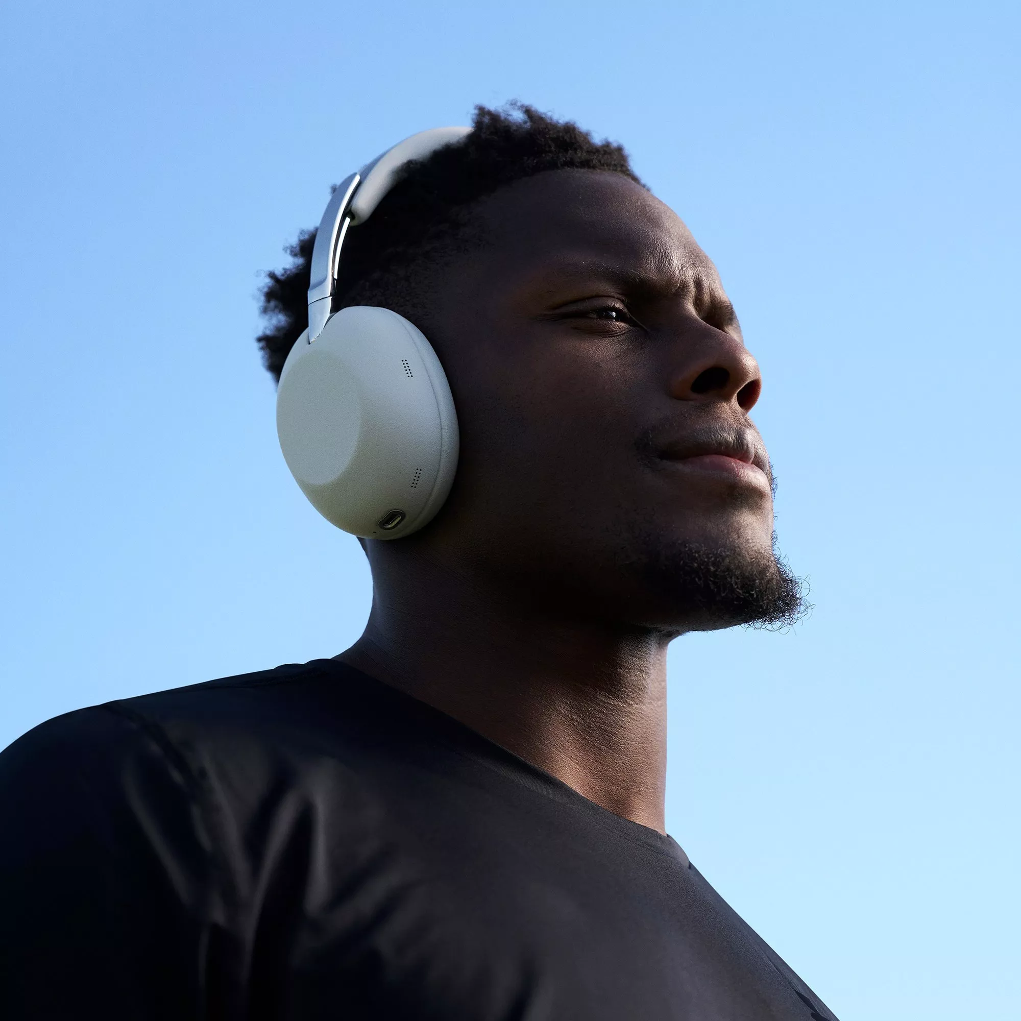 Low-angle portrait of man wearing white over-ear headphones and black T-shirt against clear blue sky