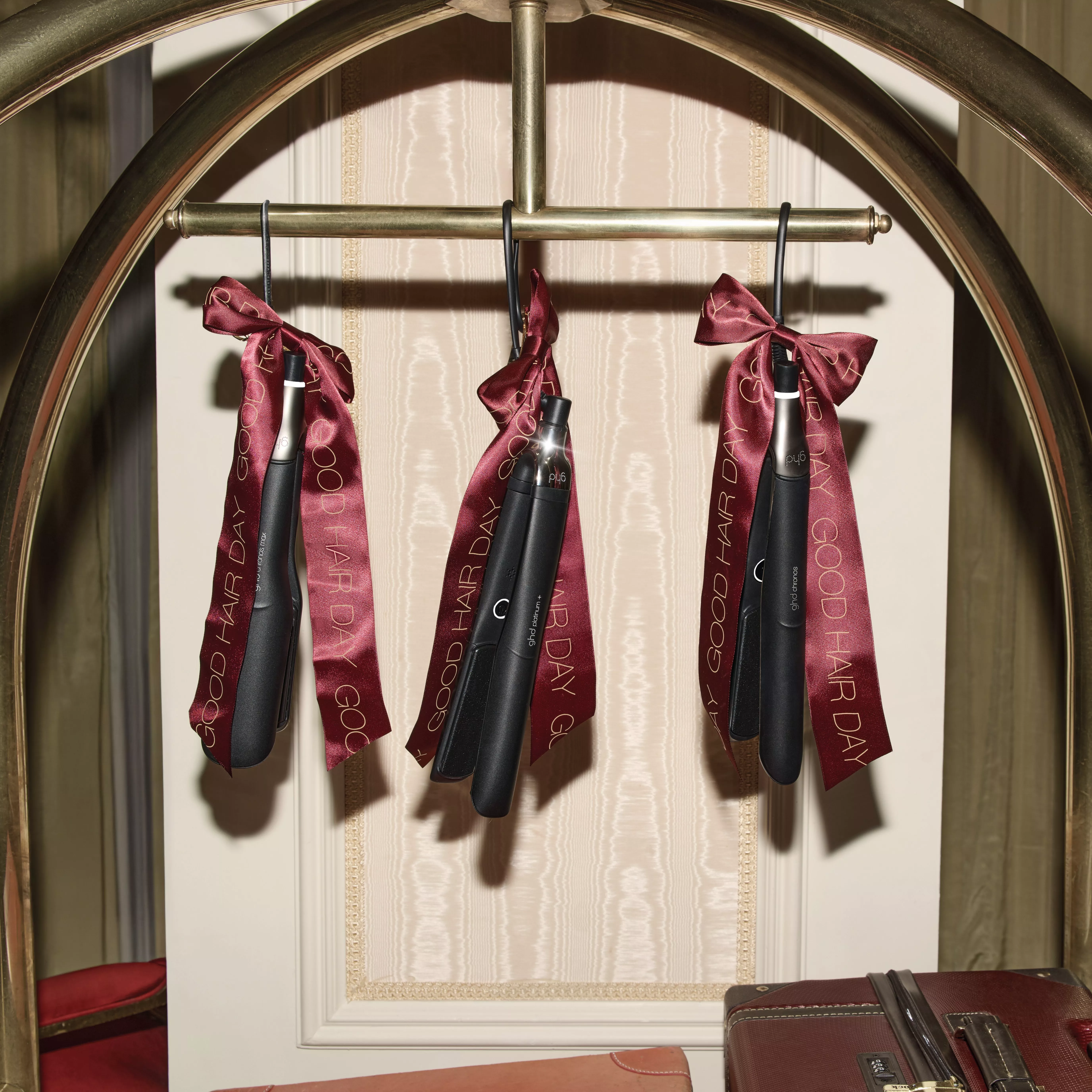 GHD hair straighteners hanging from a luggage trolley with red Christmas ribbon